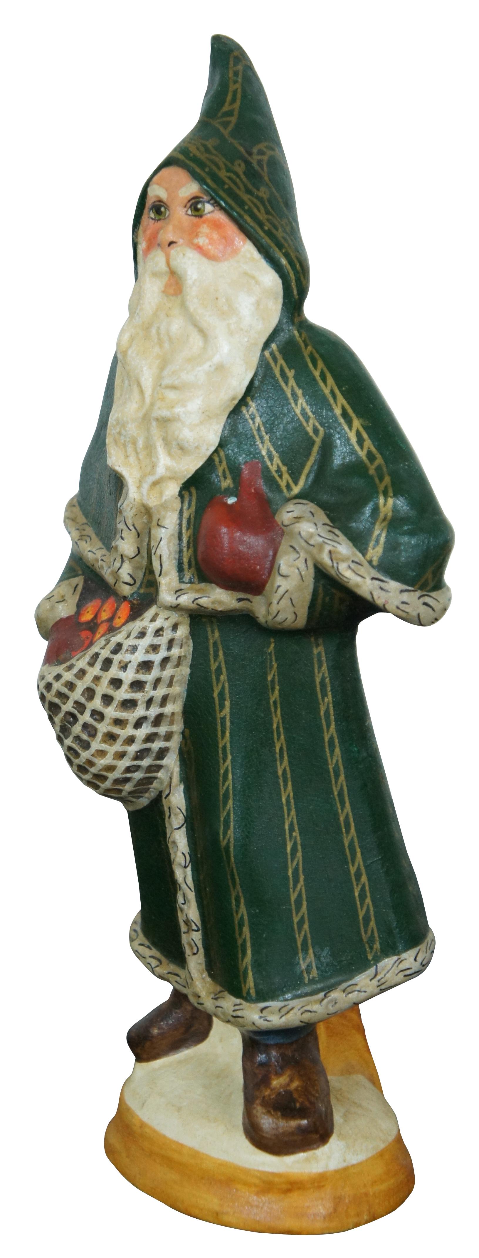 Vintage 1992 Vaillancourt Folk Art Kreidegeschirr Figur #1219 des Weihnachtsmannes oder Santa Claus in grün und gold gekleidet mit einer Schirmmütze und roten Handschuhen, trägt einen gewebten Sack mit Obst, wahrscheinlich Äpfel.
 