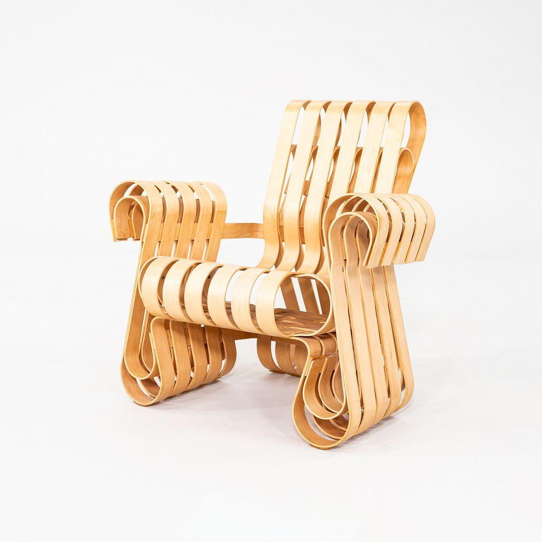 Se trata de una Silla Power Play Lounge, diseñada originalmente por Frank Gehry para Knoll en 1992. Este ejemplo concreto se fabricó en Estados Unidos y data del año 1993. La forma escultural presenta cintas entrelazadas de madera contrachapada de
