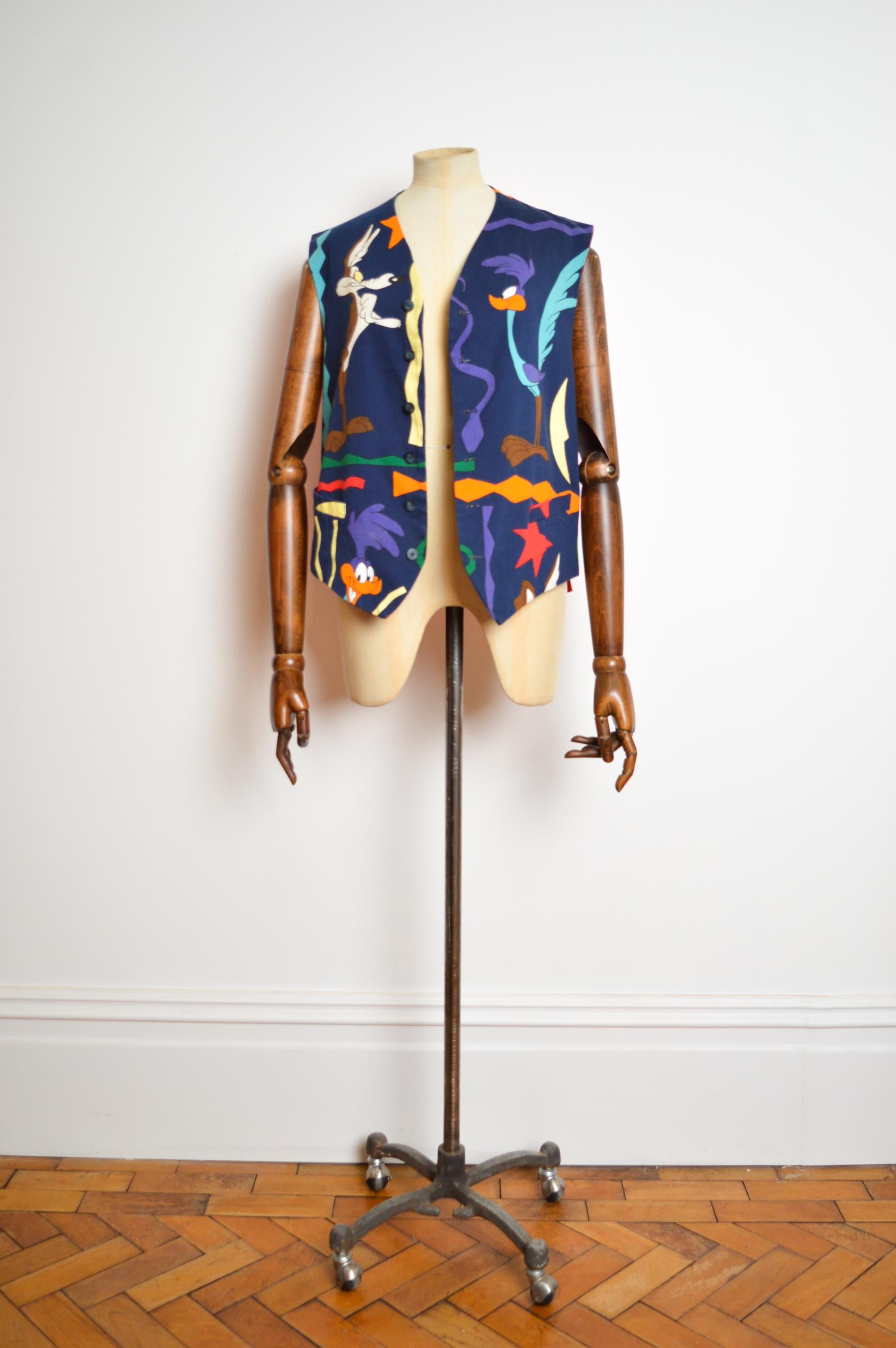 A Fun 1993 Vintage Jean Charle de Castelbajac Collaborative Warner Brothers 'Road Runner' Vest depicting Wile E. Coyote and the Road Runner, the famous duo of cartoon characters from the Looney Tunes show.

MADE IN ITALY.

Measurements provided in