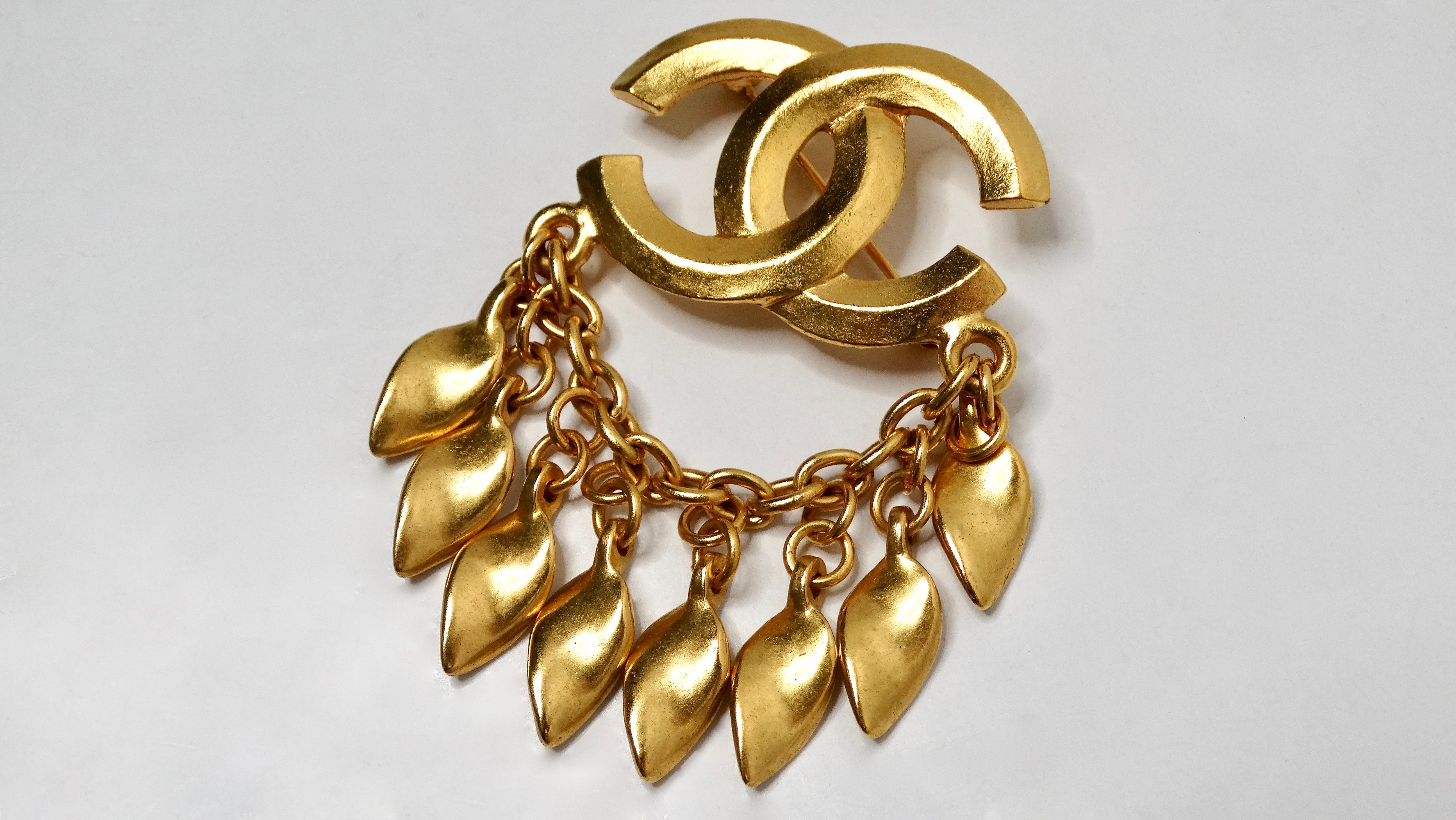 The 1996 Chanel Coco Mark Yellow Gold-Tone Brooch with Dangling Charms is an exquisite accessory that elegantly embodies the essence of luxury and sophistication. This striking piece features a gold-tone interlocking CC emblem, symbolizing Chanel’s