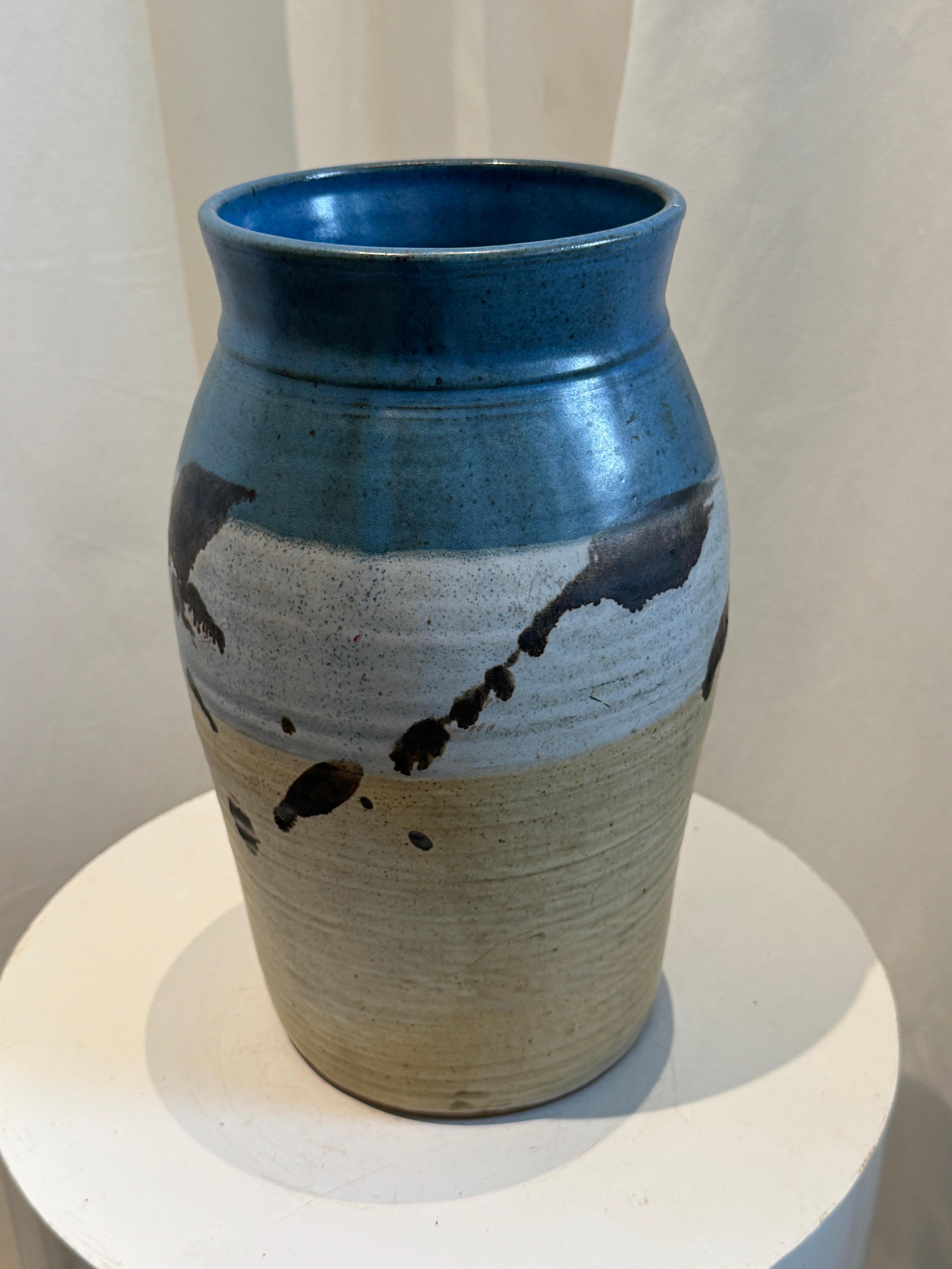 This exquisite handcrafted studio pottery vase, signed and dated M. Hainest, 1996, is a striking example of artisanal ceramic craftsmanship. The vase features a stunning gradient glaze, transitioning from a soft matte blue at the top to a speckled