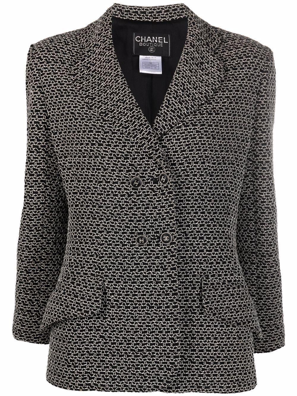 Chaqueta Chanel de tweed boucle negro con doble botonadura, red de punto blanca, botones de fantasía con el logotipo y forro de seda. 
Alrededor de 1998. 
Ver imagen de pasarela adjunta.
Composición: Lana 51%, viscosa 44%, nailon 5%.
Forro: Seda