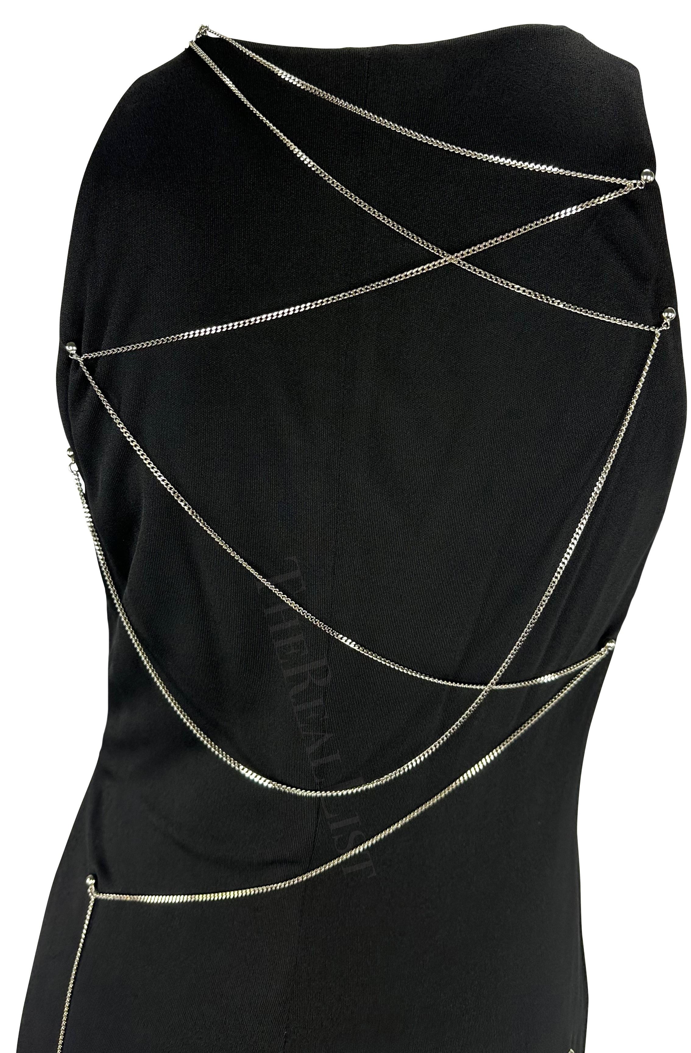 Présentation d'une robe en maille noire de Gianni Versace, dessinée par Donatella Versace. Datant de 1999, cette robe présente un décolleté en V doublé d'une chaîne argentée. Le dos de cette robe est complété par une chaîne argentée assortie qui se