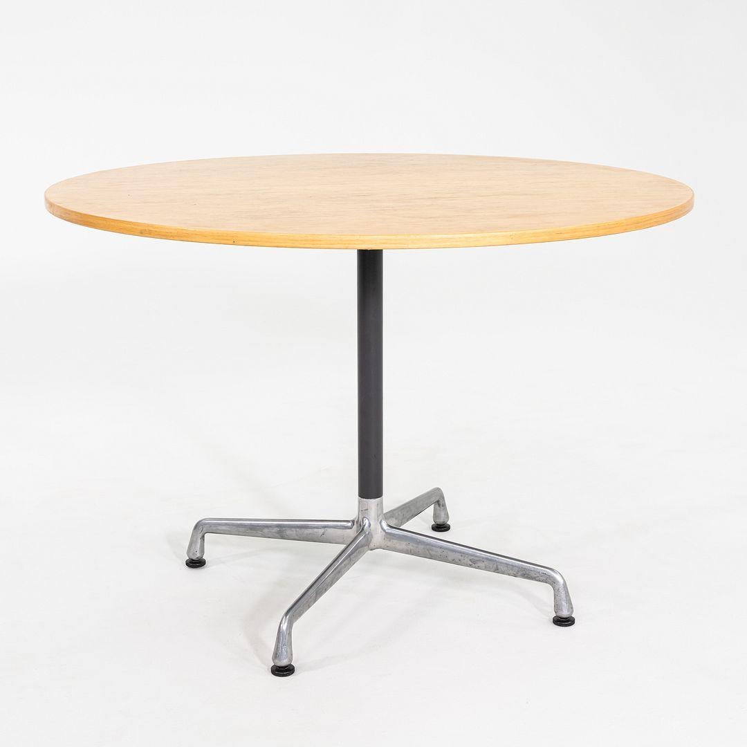 This is an Eames Aluminum Group Cafe / Dining Table, originally designed by Charles and Ray Eames in 1961. This particular example was produced by Herman Miller in 1999. The table features a round wood veneer top, supported by a classic Eames