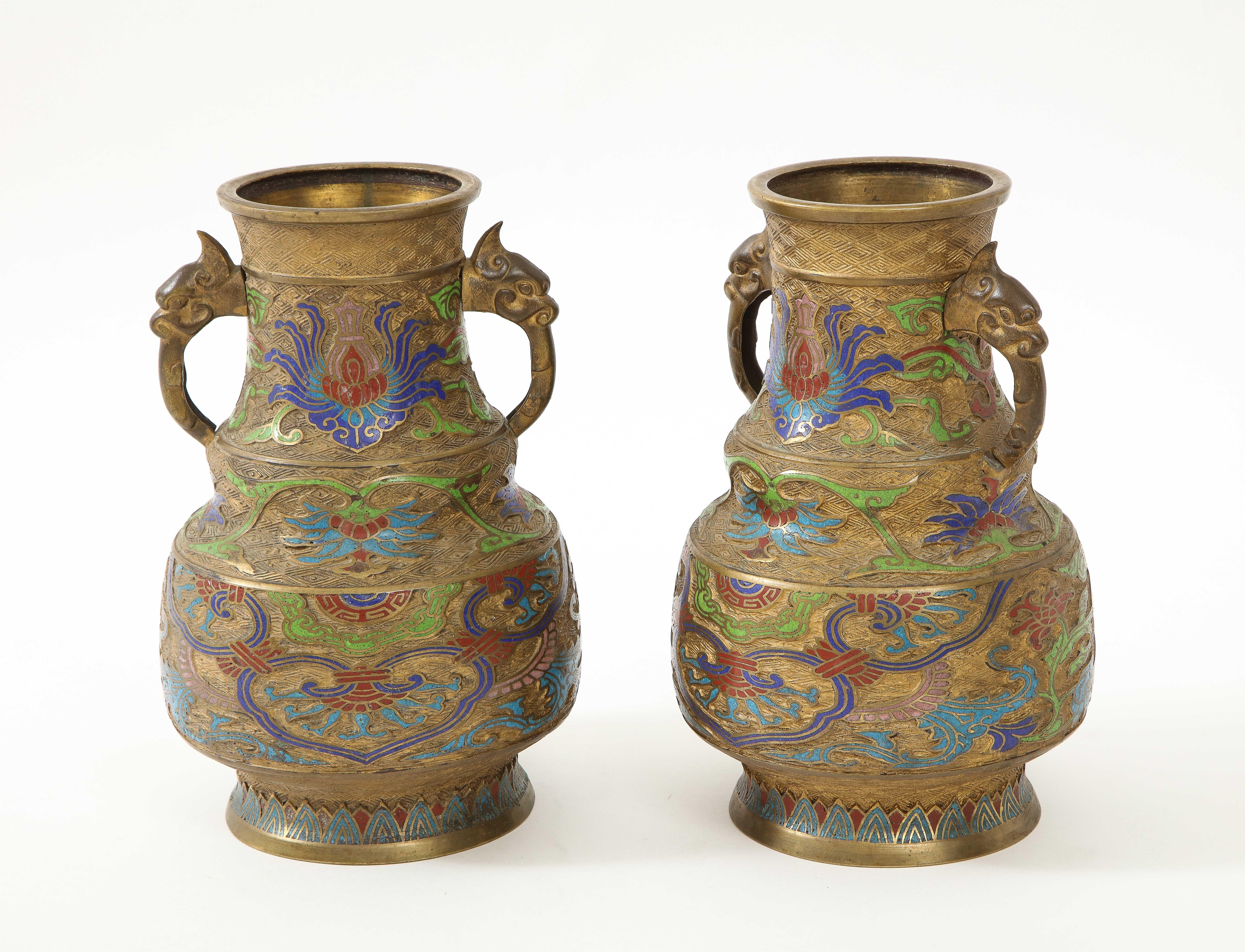 Pair of Chinese export late 19th century cloisonne vessels. Vessels feature hand chased glass stylized floral patterns in Victorian era colors of red/maroon, blues and green. Dragon Handles complete the exotic appeal.