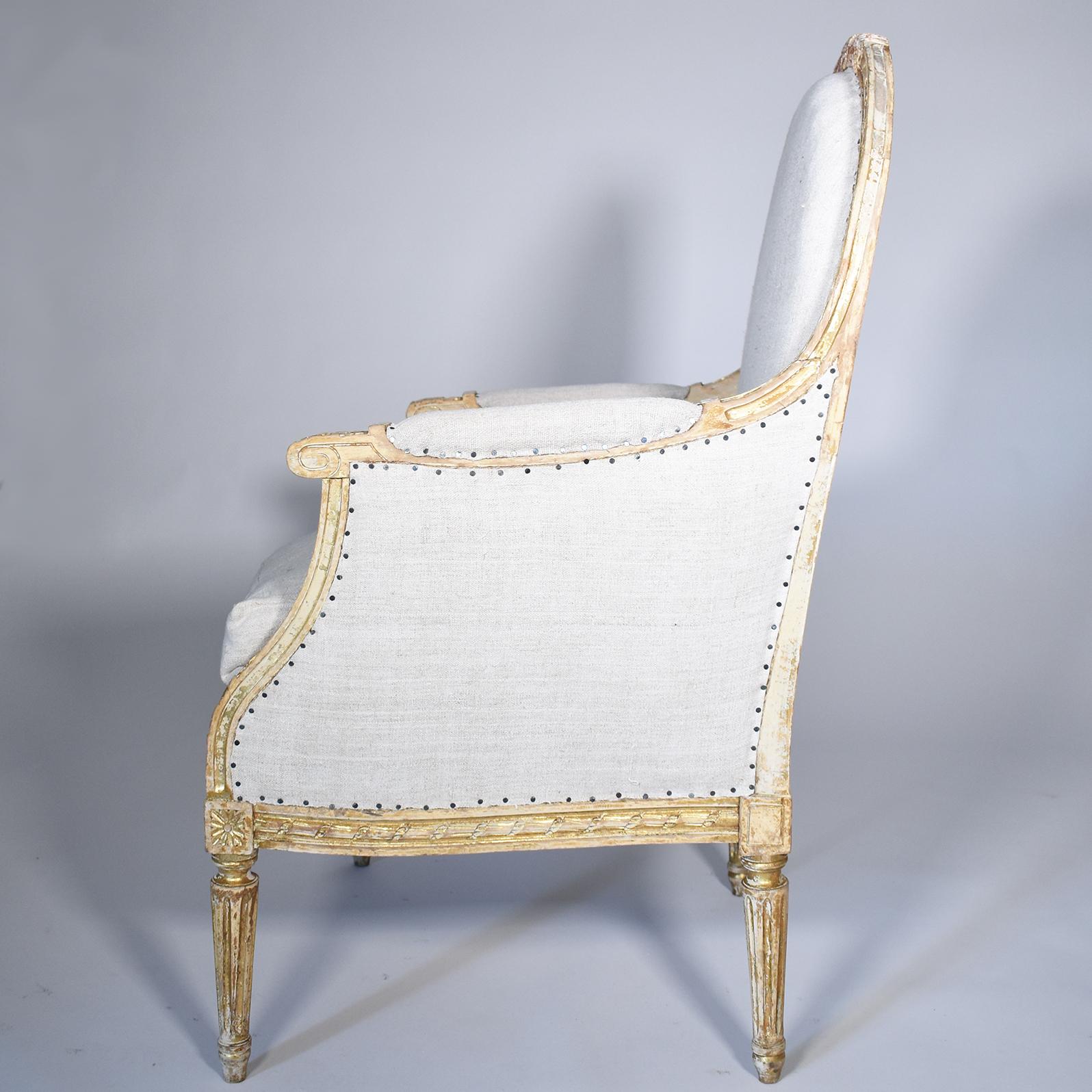Grand scale 19th century French gilded Bergère armchair has elegant carving on chair frame, apron and fluted legs. Scattered losses on gilding and carving. Upholstered in European burlap and simple nailheads.
