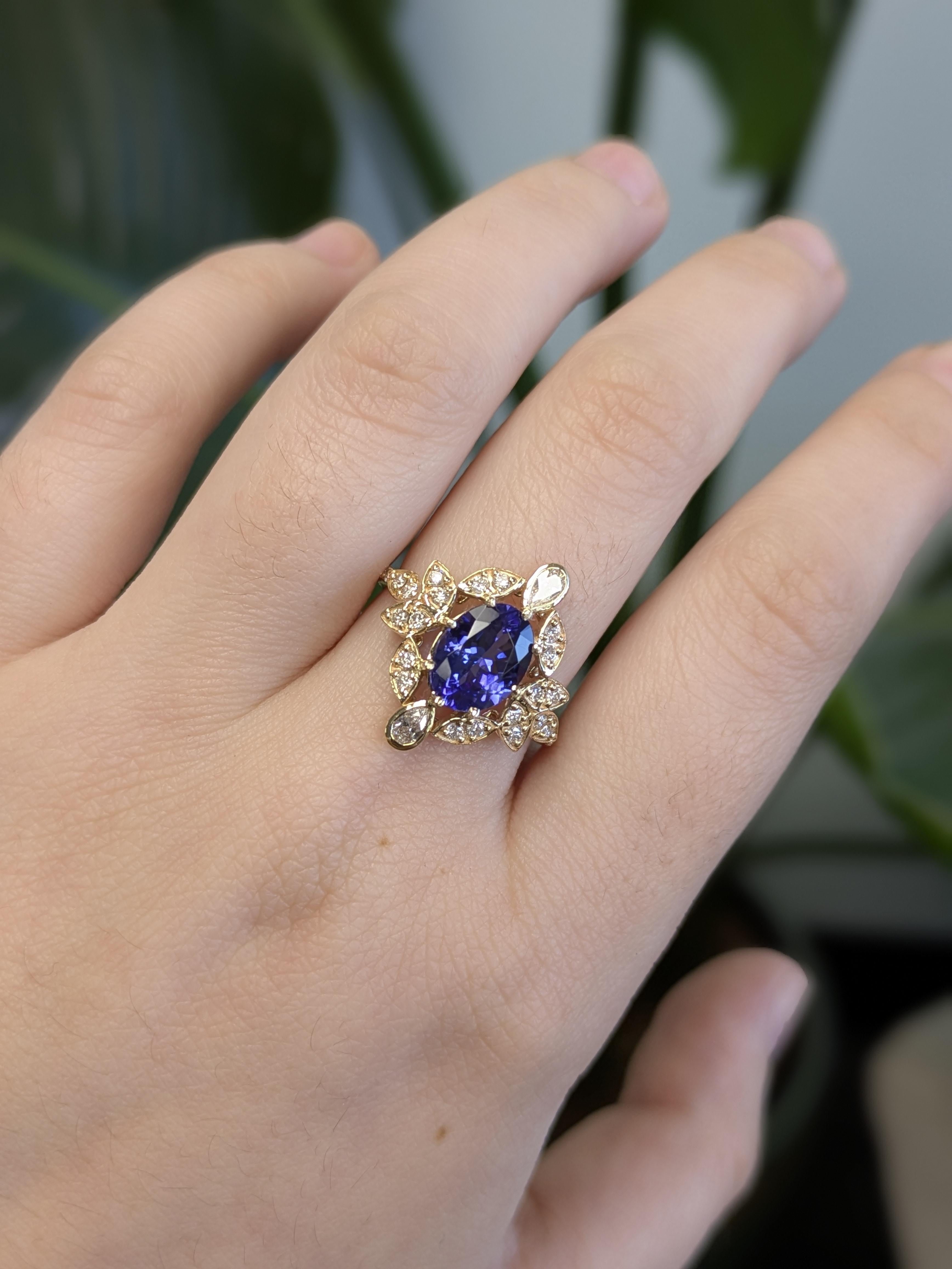 Questo squisito anello in oro giallo 14K presenta una pietra centrale di tanzanite dal taglio ovale, circondata da delicati accenti di diamanti naturali incastonati in un affascinante motivo floreale. L'oro caldo e le vibranti tonalità blu-viola si