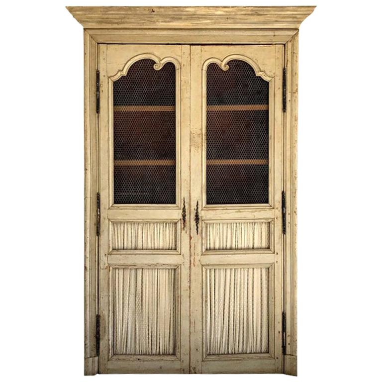 A white, brown antique French armoire made of hand carved, painted pinewood with two doors, very typical Louis XV, in good condition. Two-door paneling is partially with decorated with chicken wire, and an inside shelving. Wear consistent with age