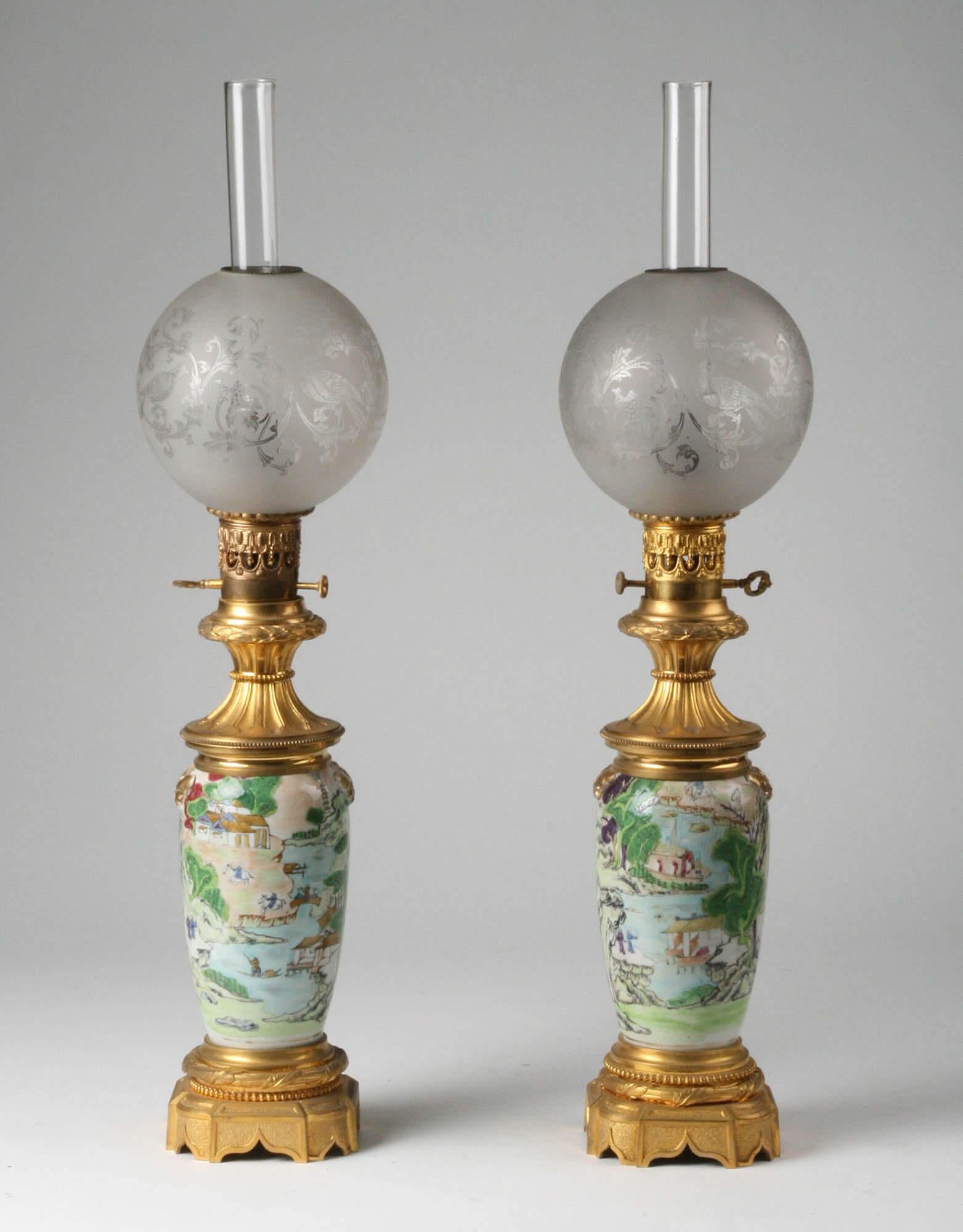 A couple of two large antique French oil lamps. Finely painted Chinese porcelain, mounted on a mercury gilt bronze. The bronzes are refined casted and chiseled. The gilding is in very good condition. On top of an engraved glass lampshade. Note: at