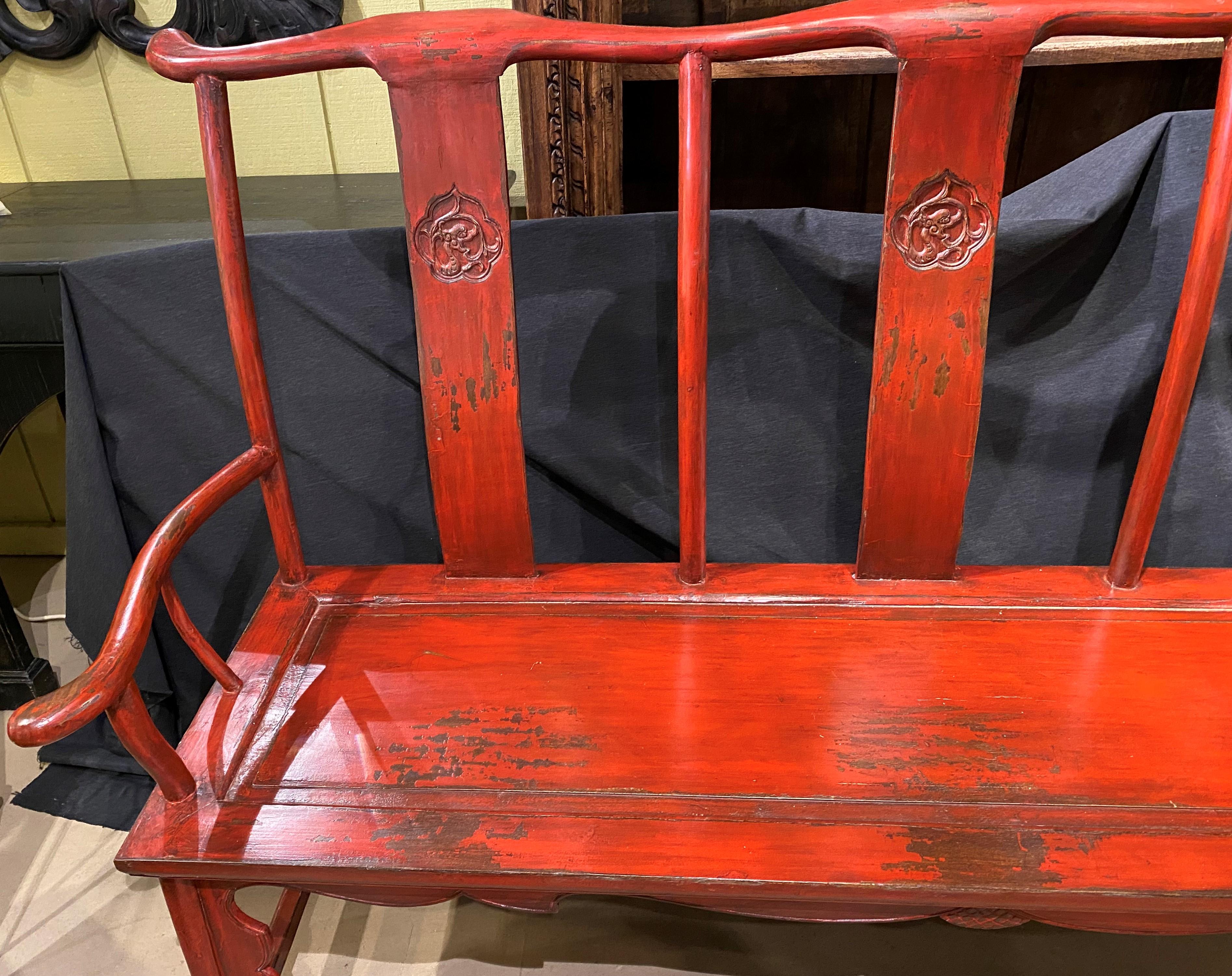 A fine example of a solid Chinese hand painted red lacquer triple seat wooden bench with curved arms, yoke crest, and carved decoration on each back splat, nicely carved skirt which continues down the front legs, and four base stretchers. The bench