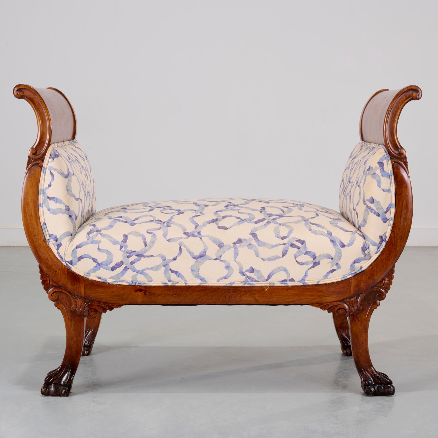 A 19th c., American Empire mahogany bench with outward scrolling arms raised on carved winged legs terminating in paw feet. The seat and sides have been newly upholstered in a striking white linen fabric printed with a flowing blue ribbon design.