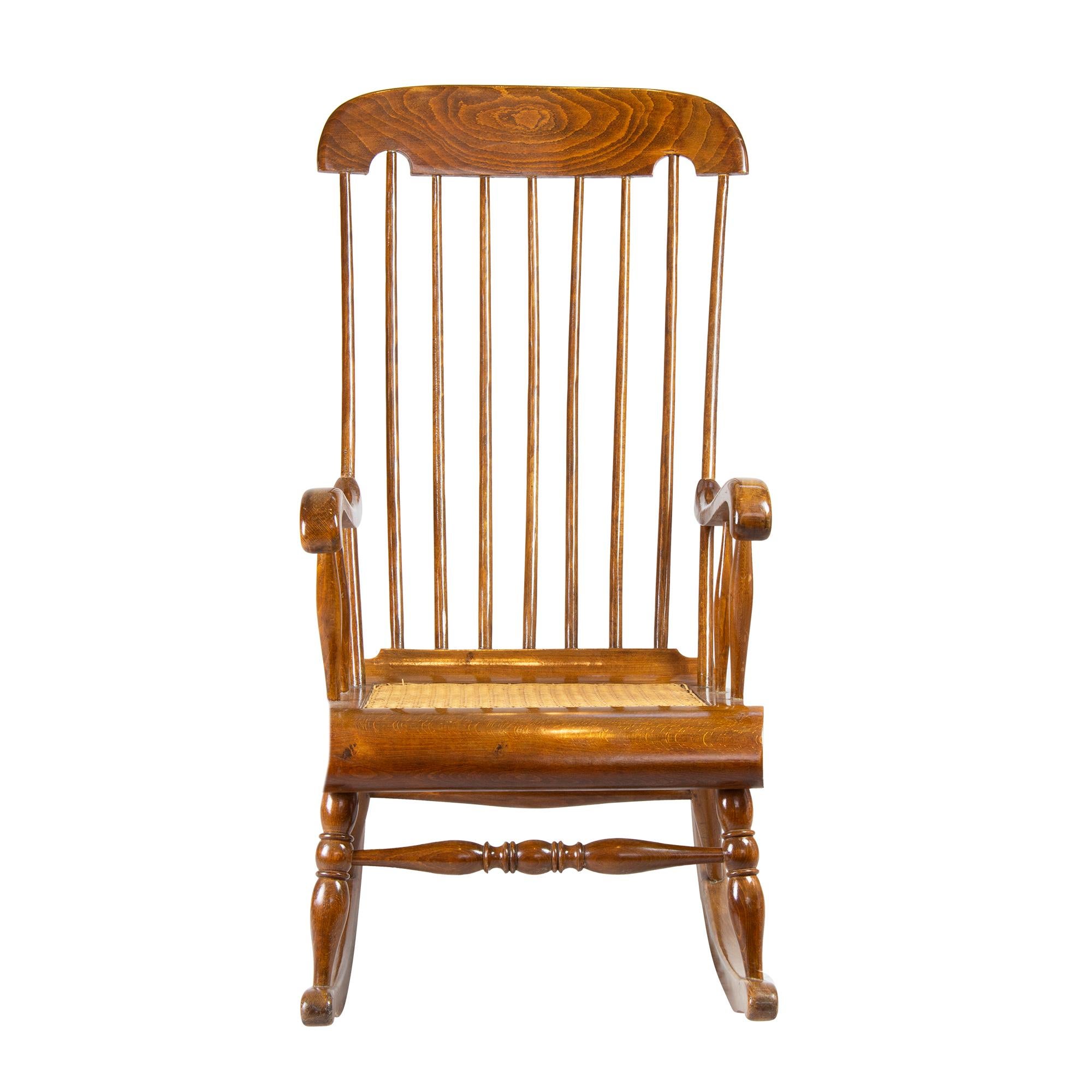 Der Armlehnen-Schaukelstuhl wurde aus massivem Buchenholz gefertigt. Die Sitzfläche ist mit Schilfrohr geflochten. Die Rücken- und Kopfstütze ist sehr weit nach oben gezogen. Der Stuhl stammt aus der Zeit um 1900.
