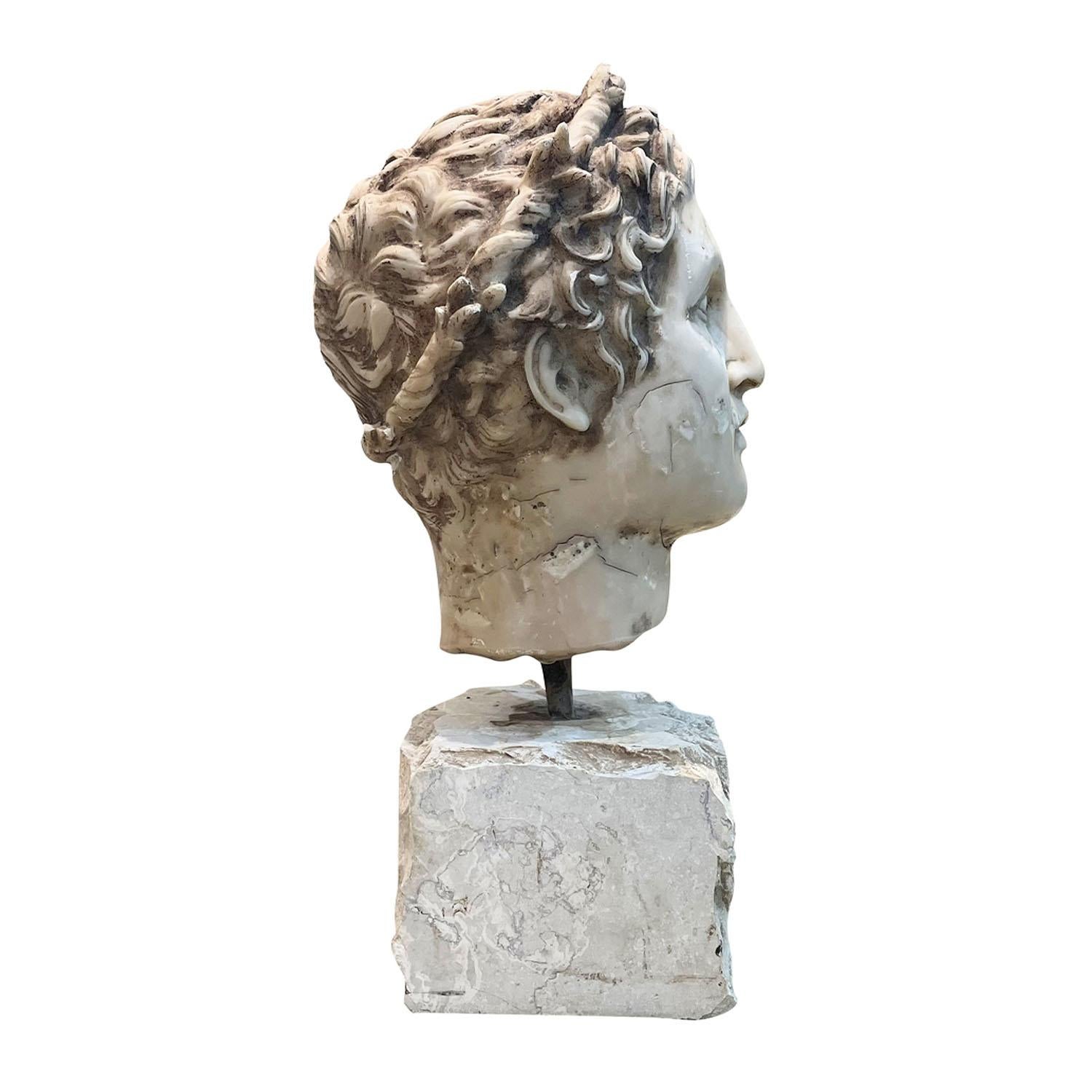 Antigua escultura italiana del siglo XIX - XX de un emperador romano con corona de laurel, realizada en mármol de Carrara tallado a mano, que descansa sobre una base tosca, en buen estado. Pequeño desteñido, debido a la edad. Desgaste propio de la