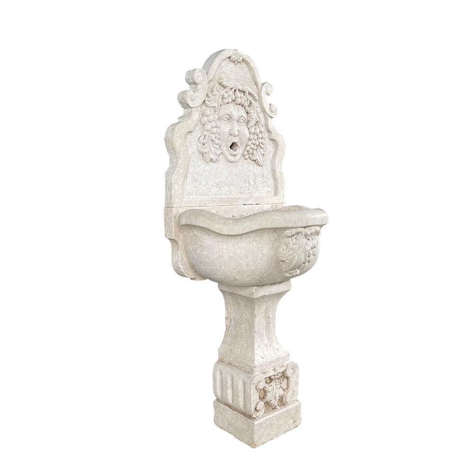 Fontaine murale italienne ancienne de la fin du XIXe siècle, sculptée à la main dans du marbre d'Istrie, en bon état. Le bassin est orné d'une grappe de raisin finement travaillée et le dosseret arqué présente des volutes latérales avec un masque de