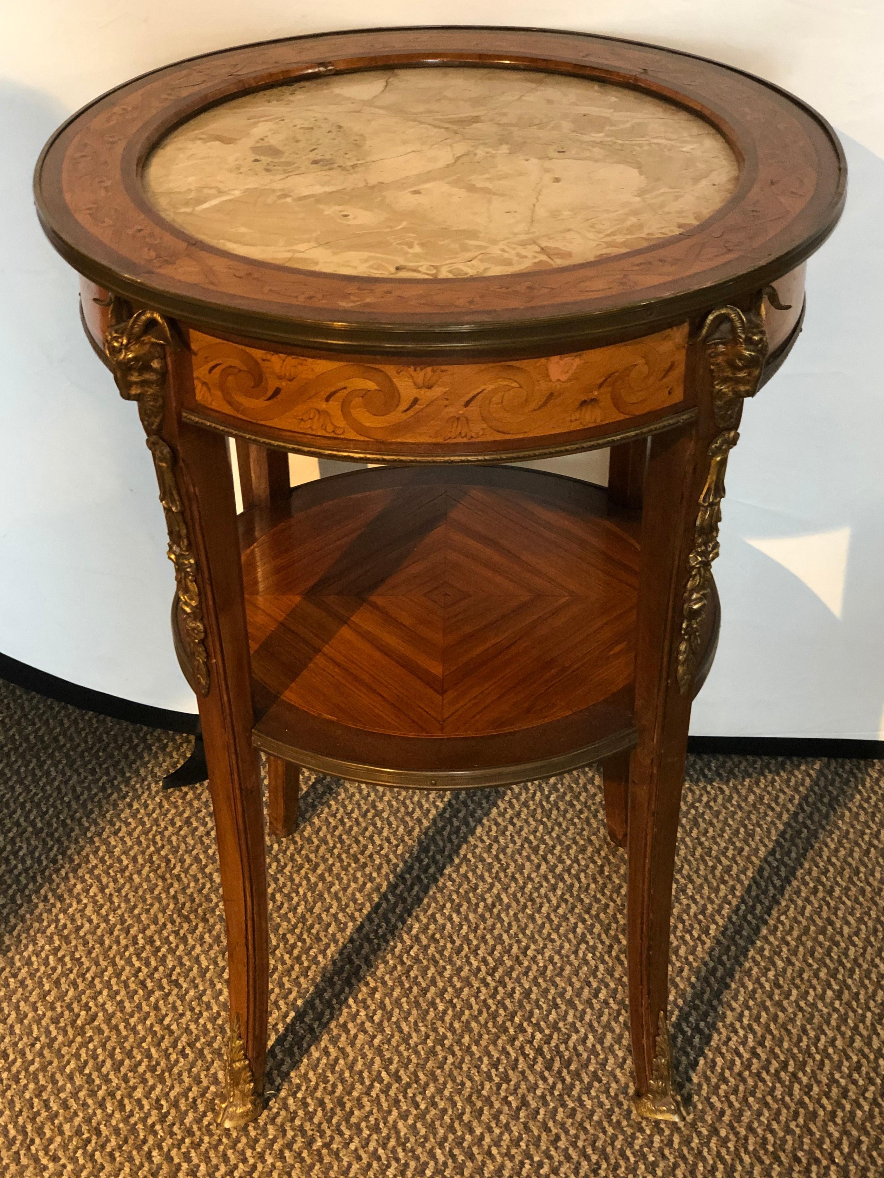 19th-20th century rams head marble top end, lamp or center table. This side table having a finely inlaid satinwood design supporting a marble top and wonderful bronze mounts with four ram heads on the circular corners. Having two full bronze shoes.