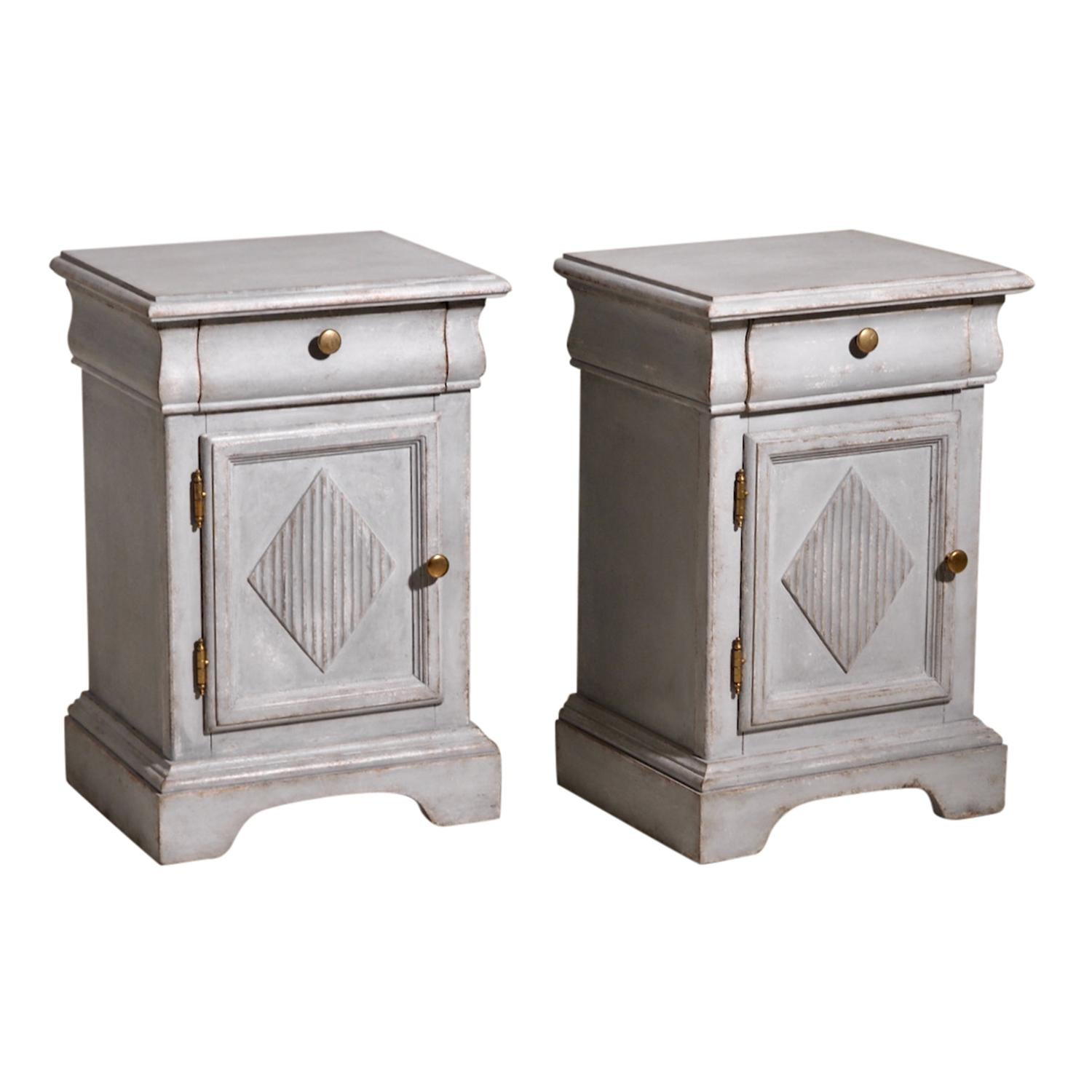 A light-grey, antique Swedish Gustavian pair of pedestal cabinets, bedside tables made of hand crafted Pinewood, in good condition. The small Scandinavian nightstands are composed with one upper drawer and a door, enhanced by detailed wood carvings.