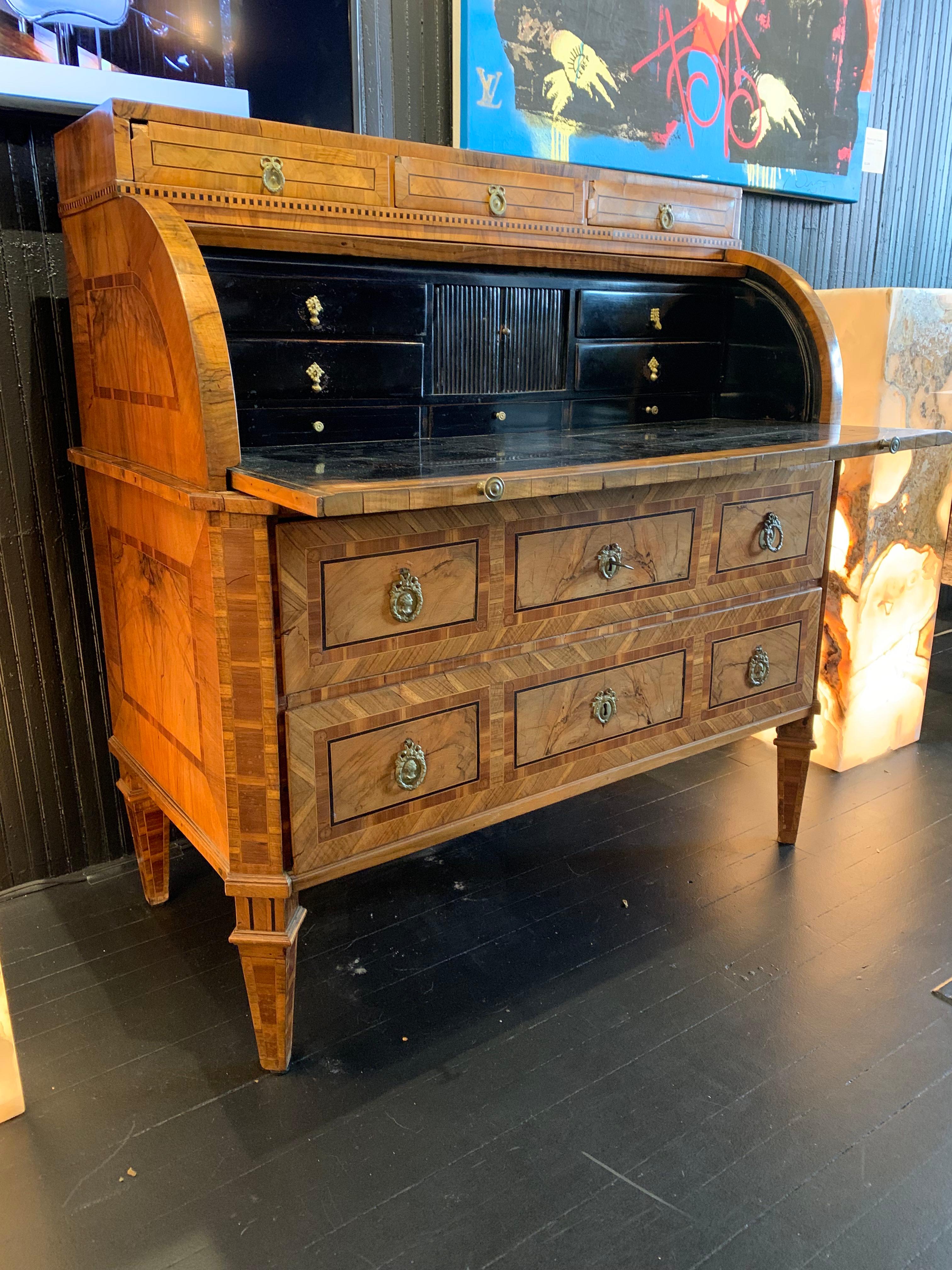 Handcrafted marquetry inlaid cylinder desk with original brass hardware. The marquetry inlay is burled book match veneer encased in geometric inlays. The casework below sits on tapered spade legs and includes two large drawers. The roll-top cylinder