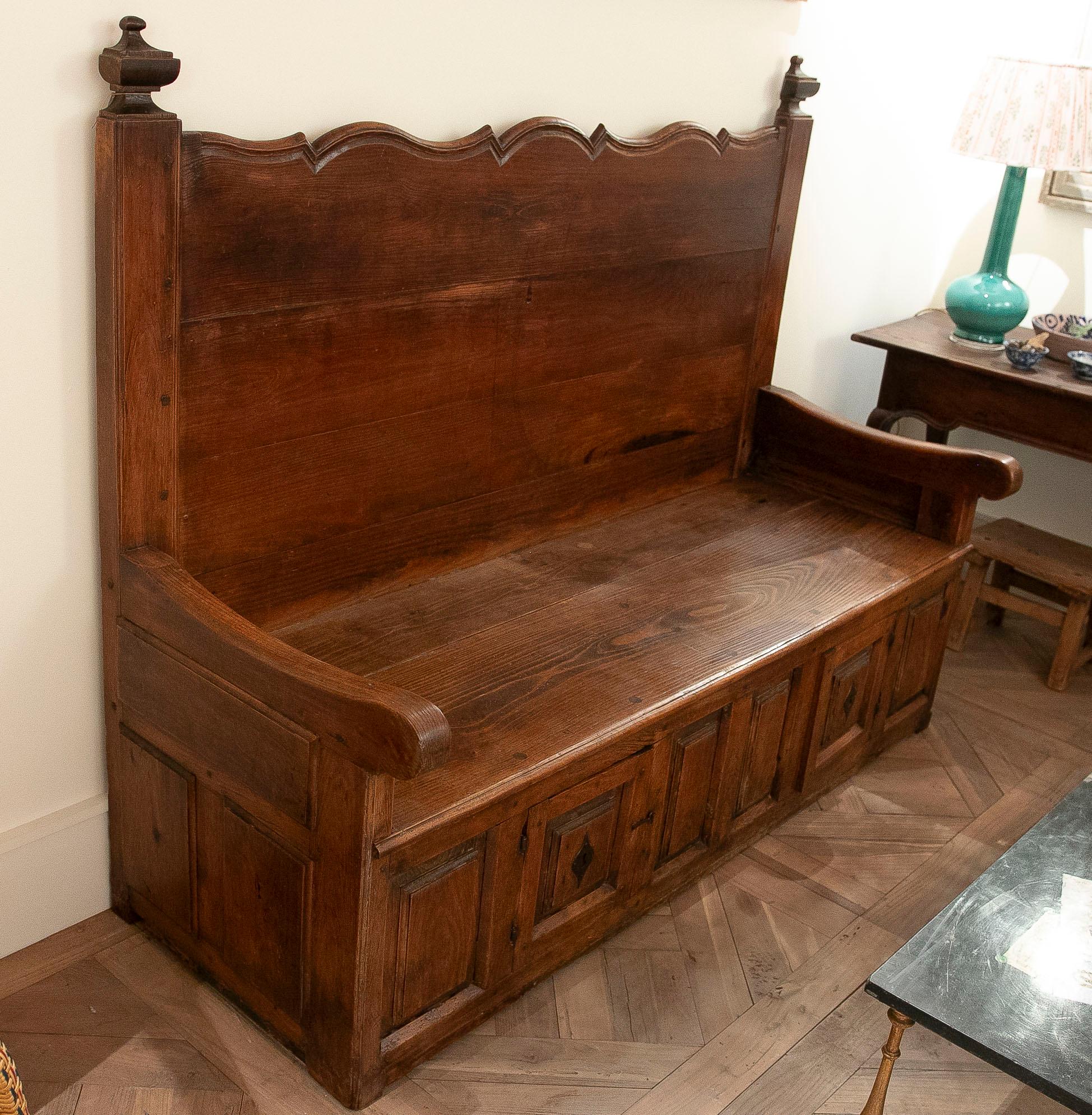 Superbe banc espagnol de la fin du XIXe ou du début du XXe siècle, fabriqué en bois massif avec une patine d'origine chaleureuse. Il présente un dossier haut aux lignes sinueuses et des épis de faîtage tournés, conférant à la pièce un caractère