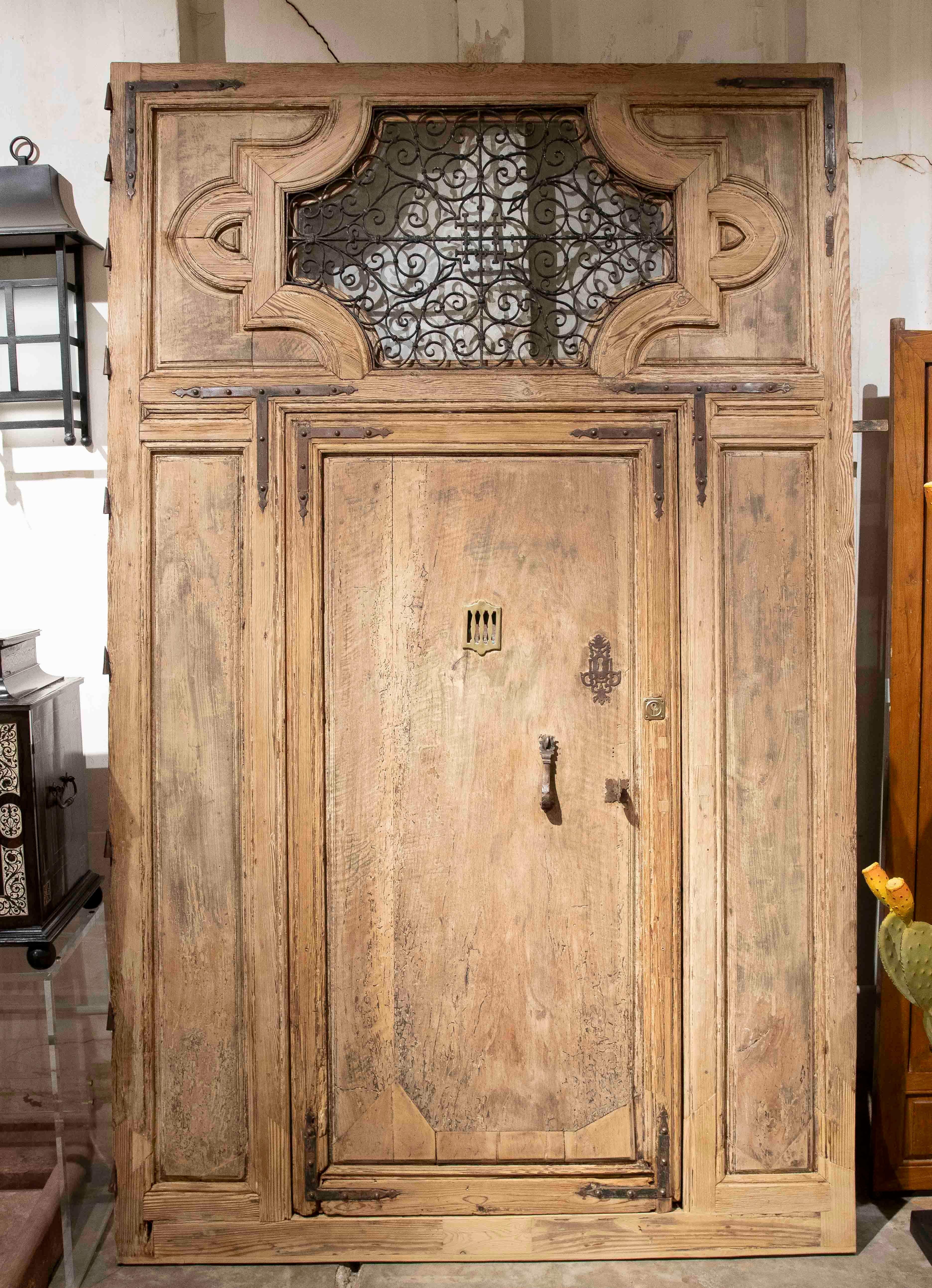 Impressive antique door made of solid wood, with a simple architectural design and handcrafted wrought iron details at the top. The piece retains its original appearance with a beautiful natural patina that reflects the passage of time. It includes
