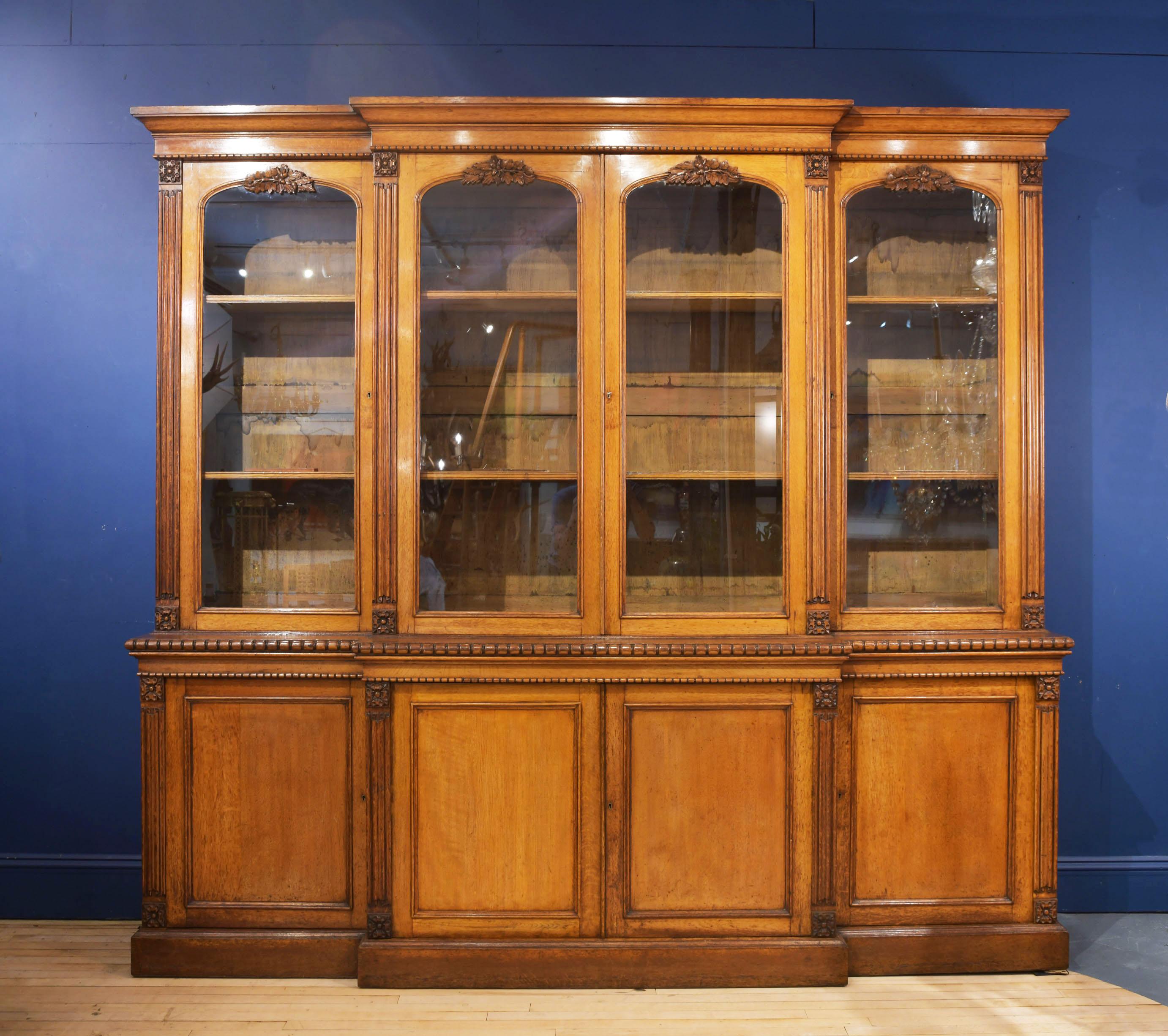 This magnificent and substantially sized English oak bookcase features linen fold carving and acorn leaf detailing above each glass panelled door. A lobe moulded edge divides the top and bottom section, both with adjustable shelves. The bookcase