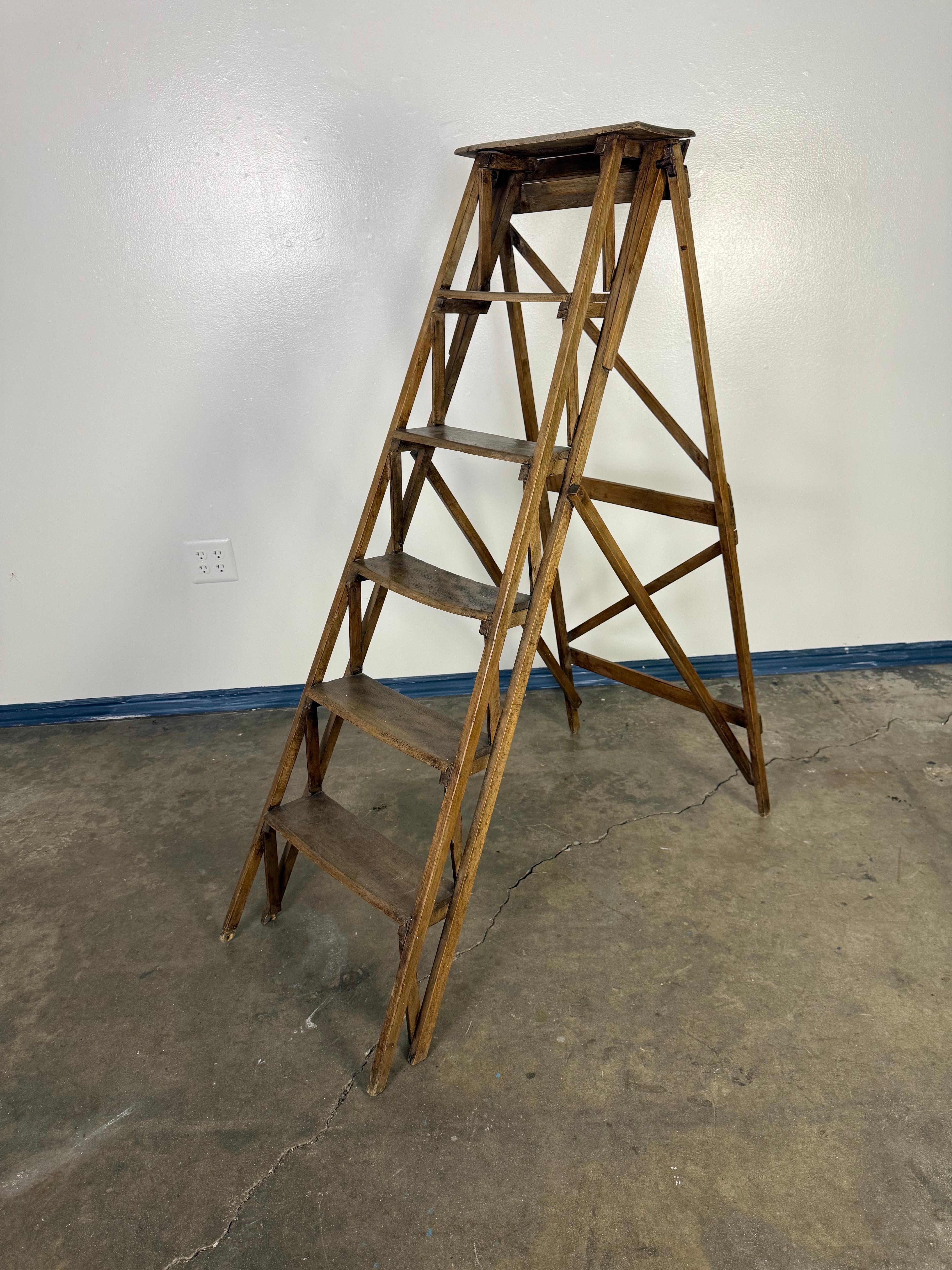 This is an antique wooden step ladder with a classic A-frame design. It features five steps, a flat top platform, and cross-braced supports for added stability. The ladder is made of aged wood with a rich, warm patina, showing signs of wear and use