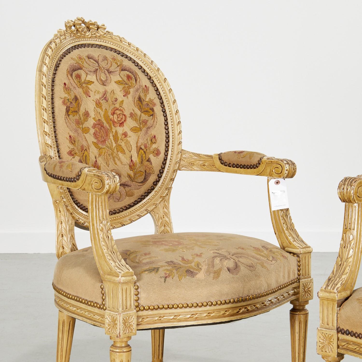 19th c., France, a lovely pair of fauteuils with painted carved wood frames, wool needlepoint embroidered upholstery and brass nailhead trim. Elaborately carved with folded ribbon crest, foliate ribbon twist back and seat rail frames. The carved and