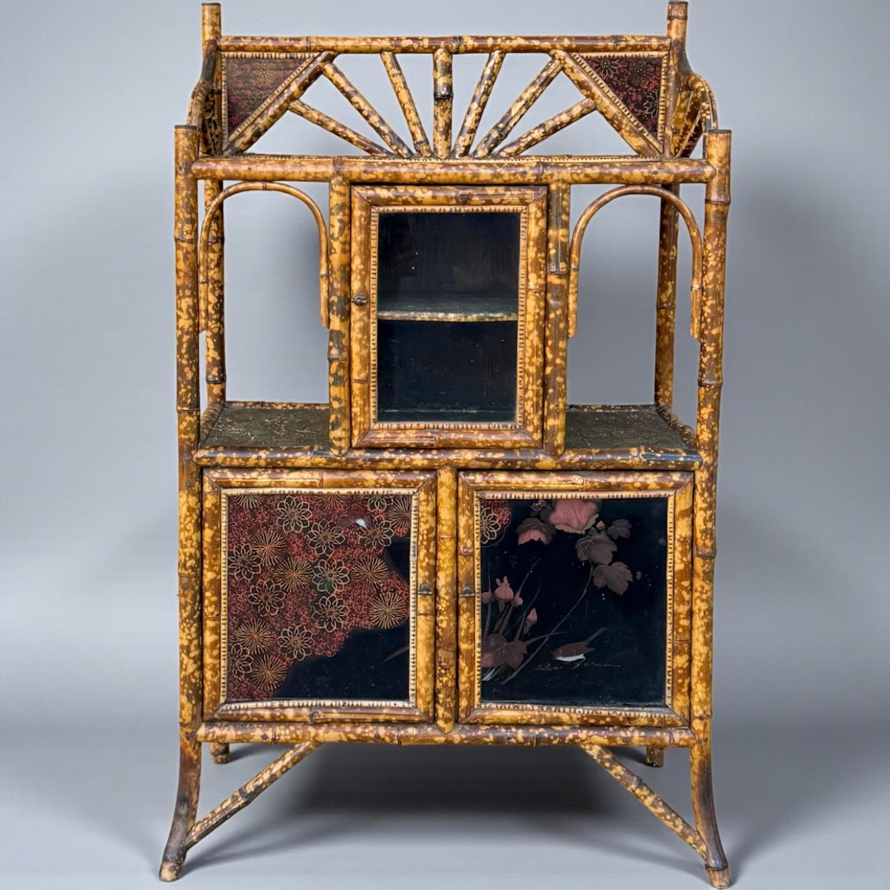 This is a wonderful example of English burnt bamboo! It is a 19th century piece with interior and exterior shelving. The sides are a green embossed paper, and the exterior panels are russet on black lacquer panels depicting birds. Nature themes are