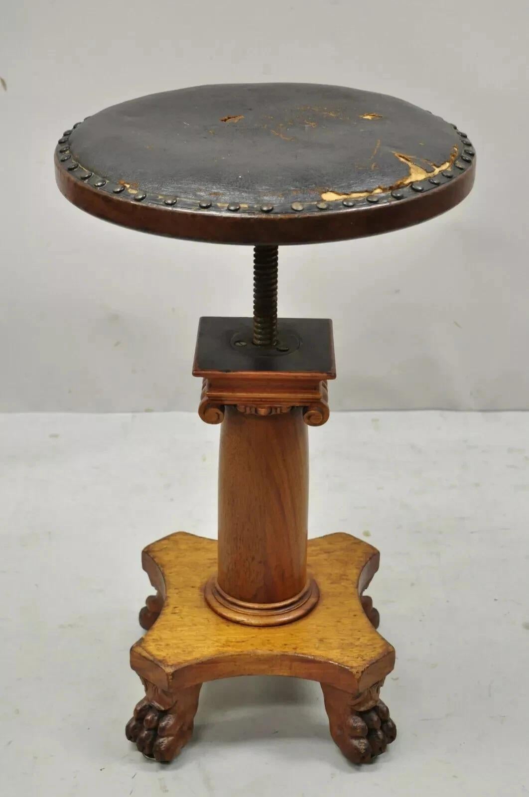 Taburete giratorio de cuero con columna de caoba tallada del Imperio Americano del S. XIX. El artículo tiene un asiento giratorio ajustable, tapicería de cuero marrón, base de columna corintia tallada en madera de caoba maciza con patas de garra