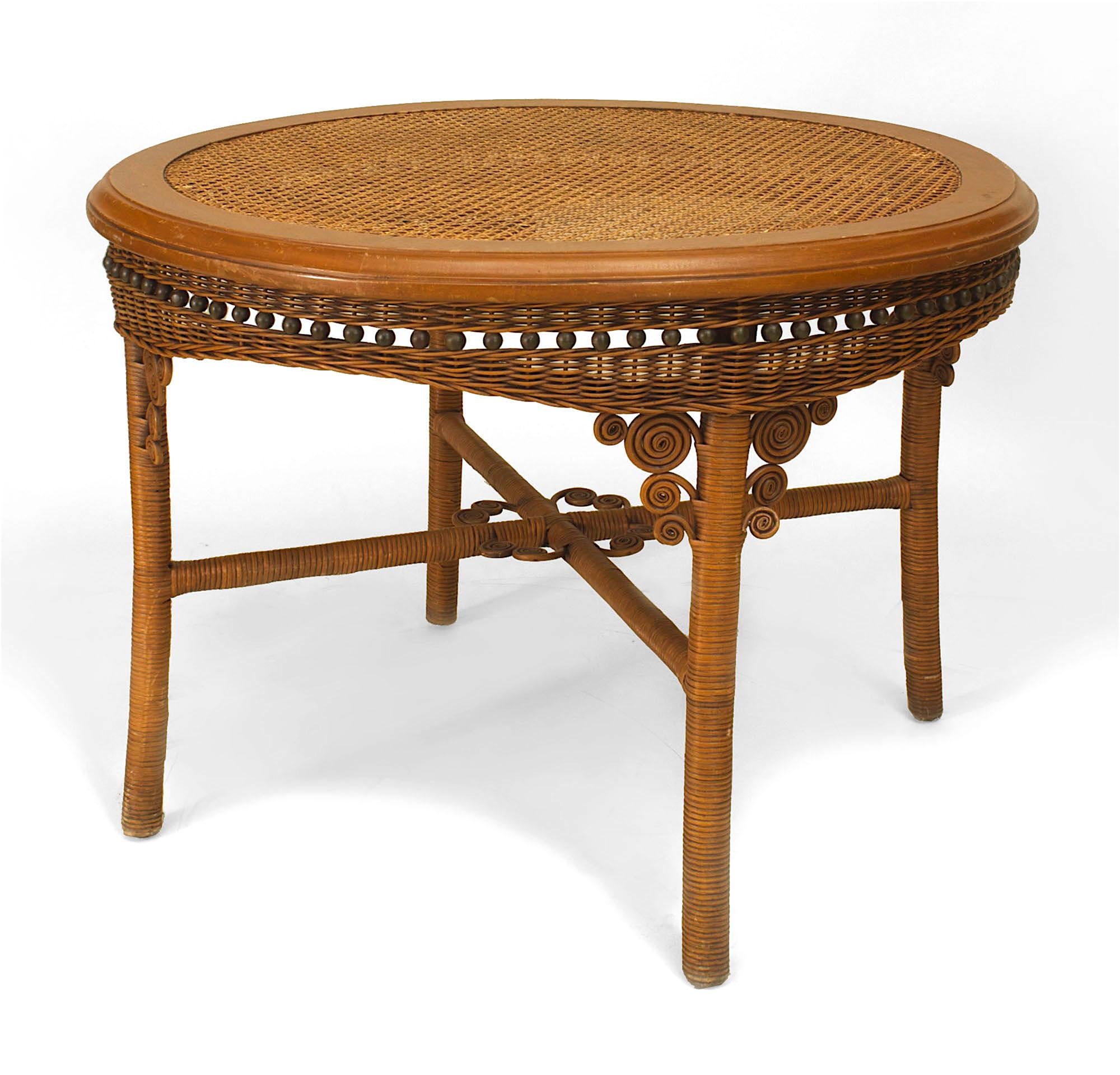 American Victorian natural wicker dining table with a round glass top over a cane surface & a woven apron with scrolls & ball design and stretcher base (Related Items: 060483)
