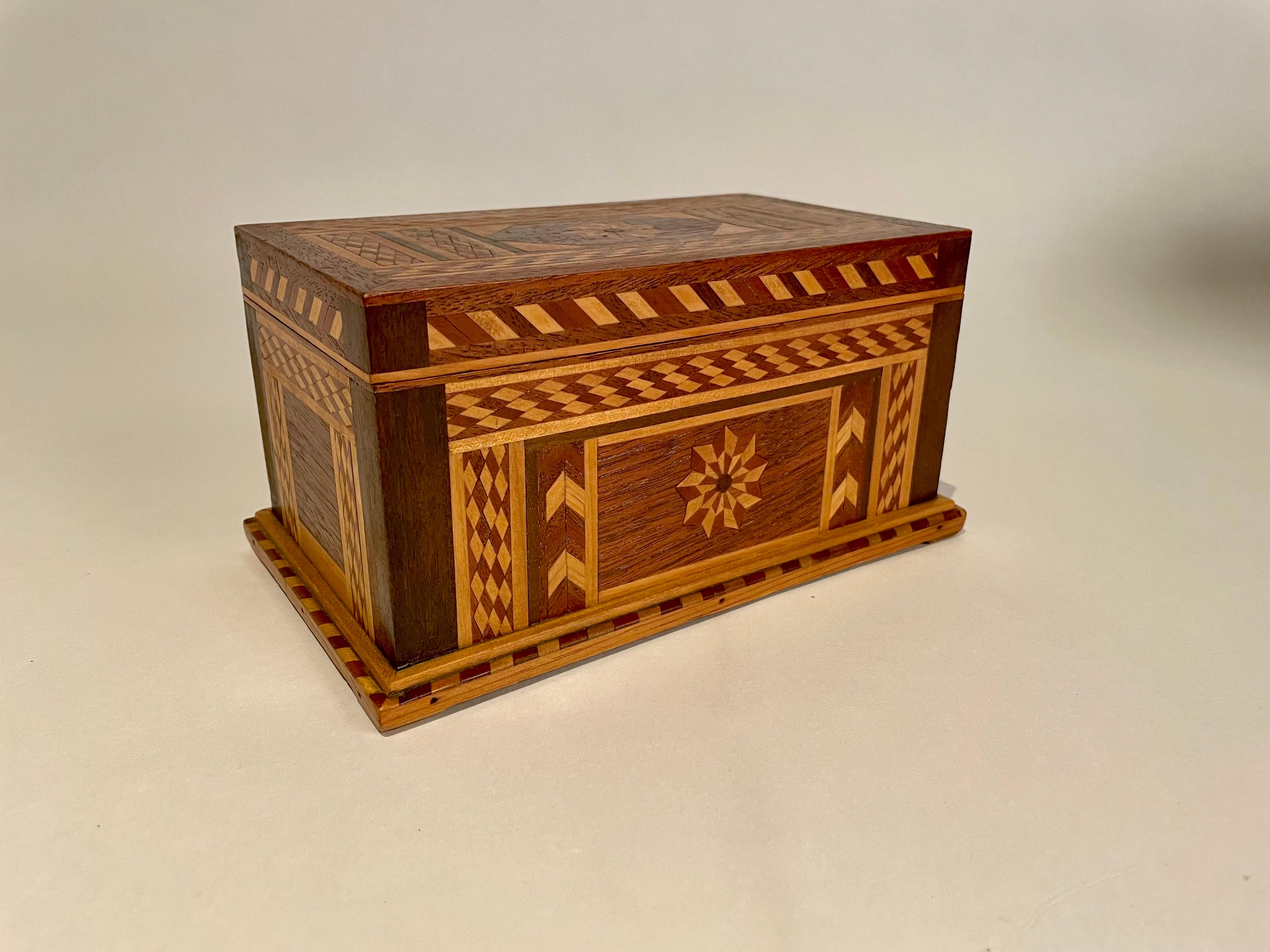 A very handsome hand crafted walnut box with wonderful geometric inlay of various fruit woods. The top and front with inlaid geometric starbursts. The rectangular desk top box resting on an integral plinth. Lined with deep purple velvet. Very fine