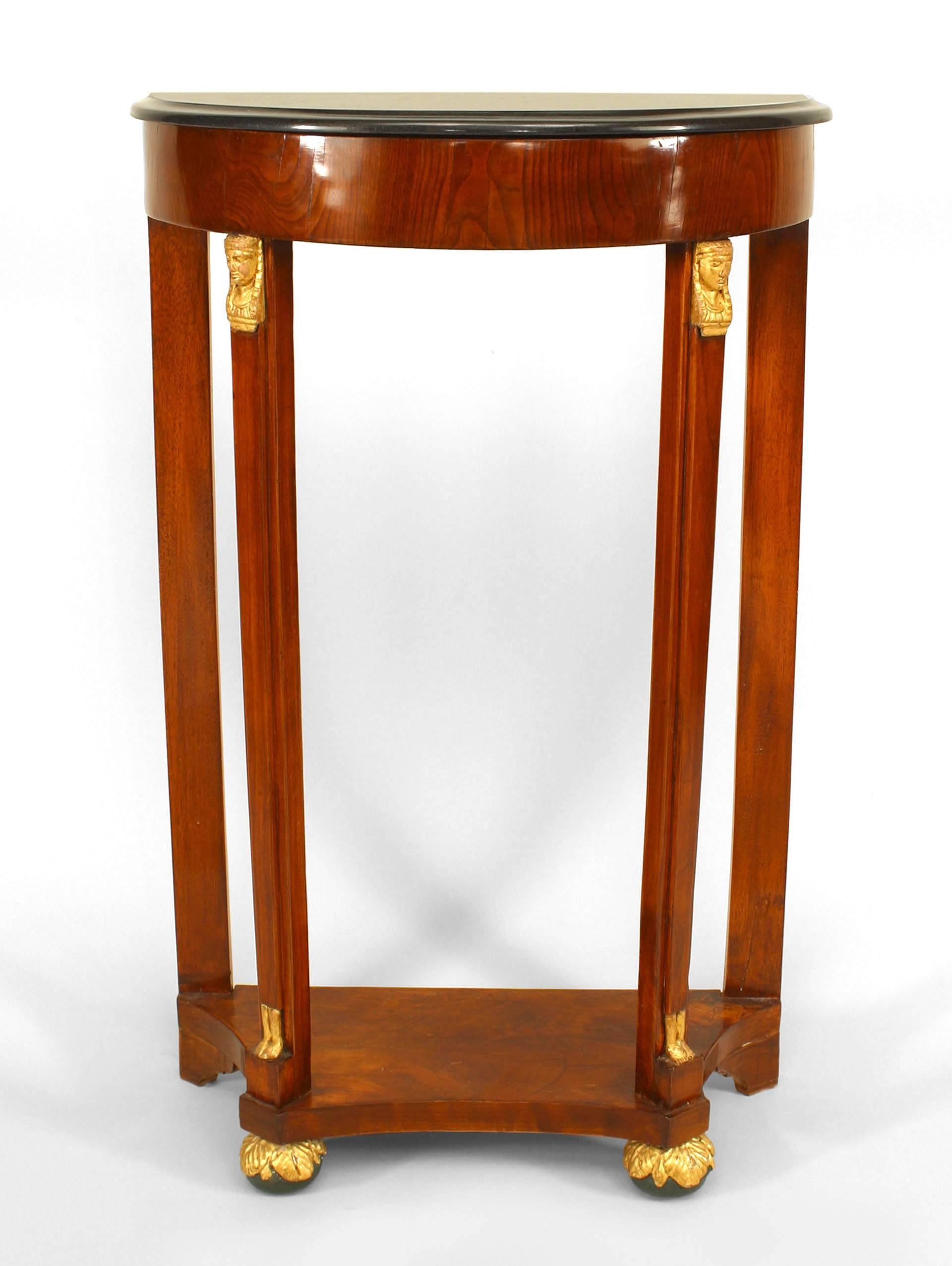 Austrian Empire console crafted circa 1830. This narrow mahogany demi-lune console feature black marble top, a platform stretcher base above ball feet, and distinctive gilt accents, such as sphinx busts and feet.