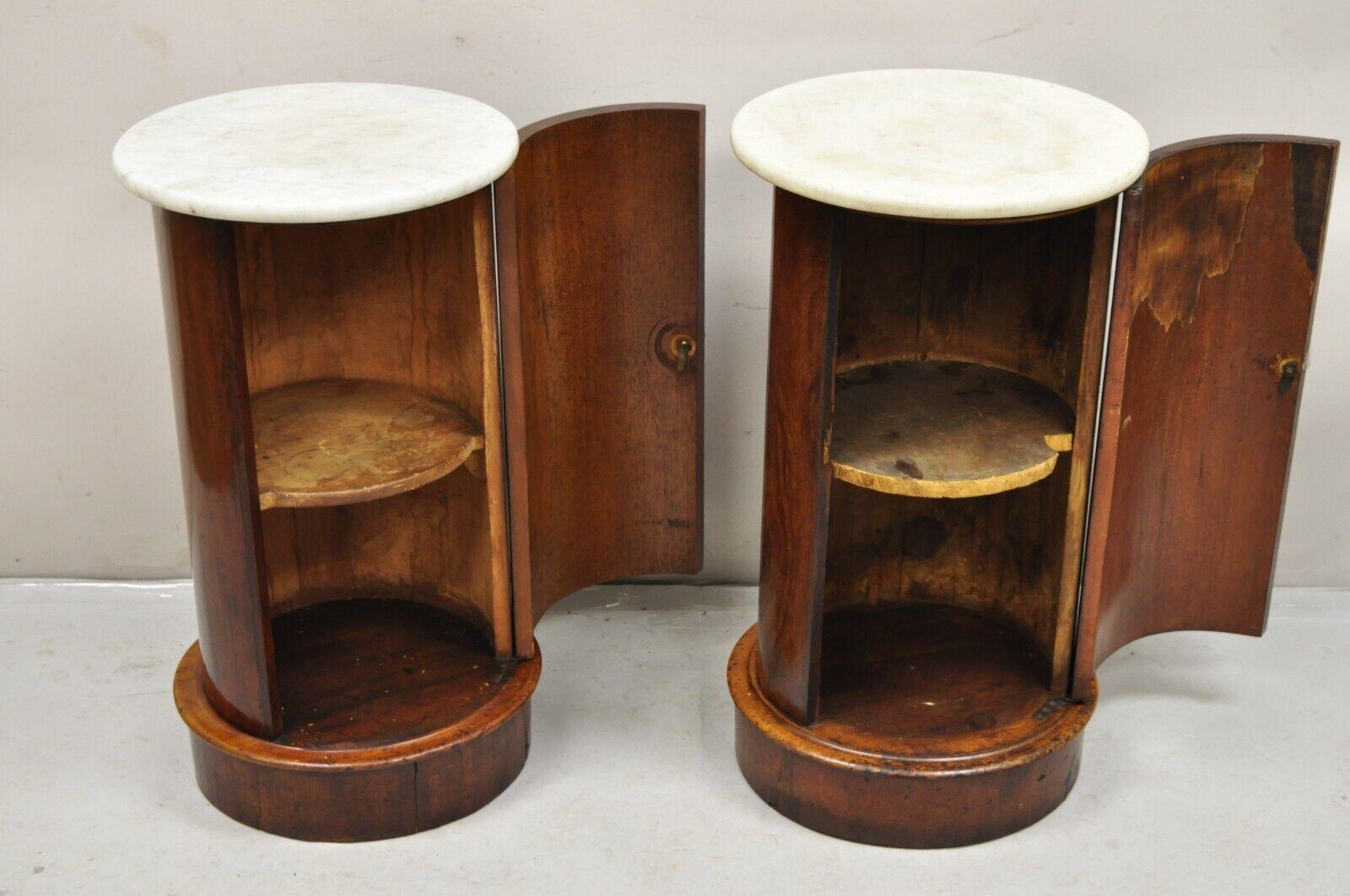 19th C Biedermeier Mahogany Marble Top One Door Side Table Cabinet - a Pair. Item features round marble tops, unique column pedestal form, beautiful mahogany wood grain, one interior shelf, very nice antique pair. Circa Mid to Late