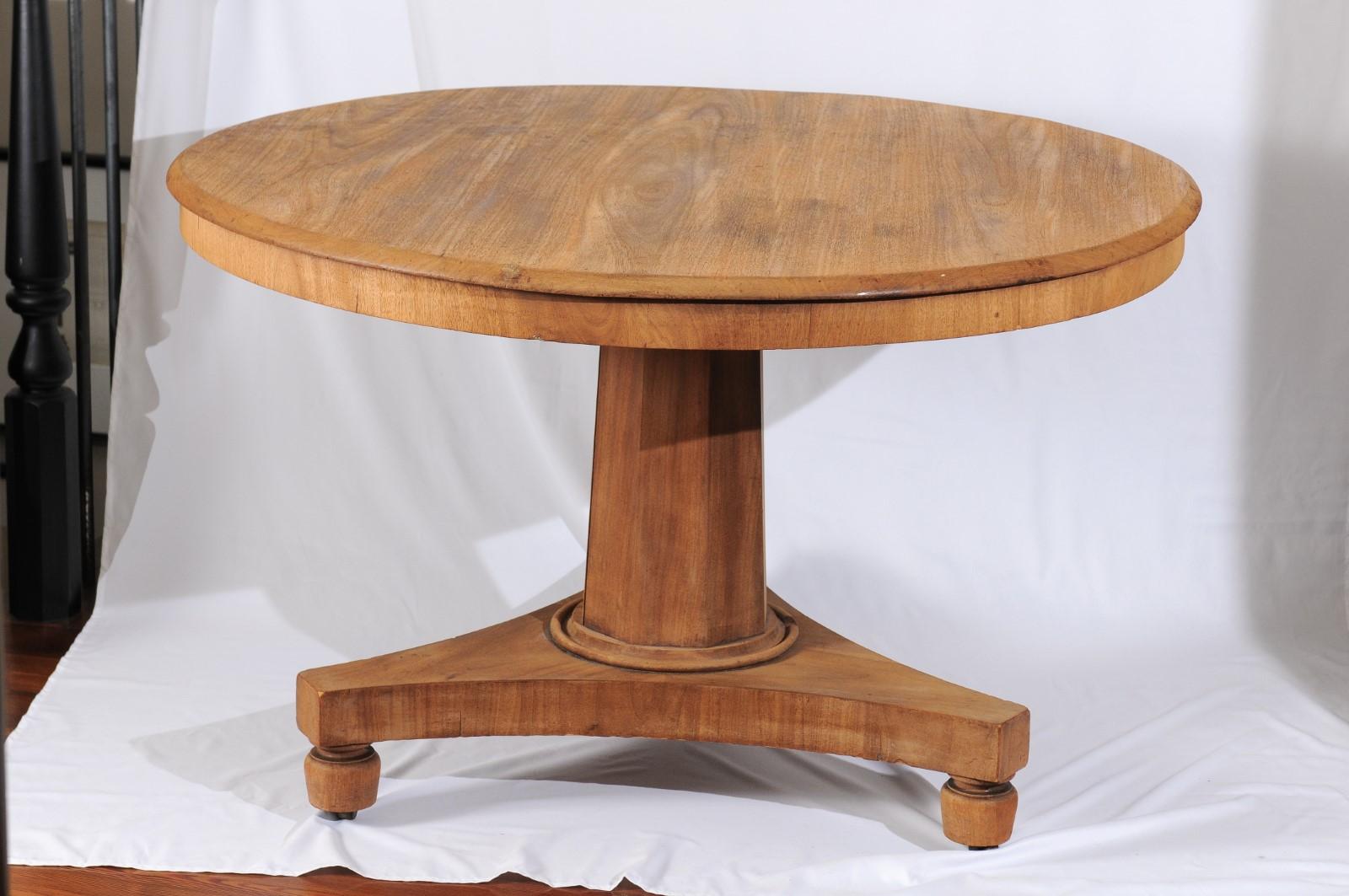 A 19th century Biedermeir-style round pedestal dining or center table featuring a round top overhanging a center pedestal with a tripod base over bulbous feet. A clear oak finish. European. Measure: 47