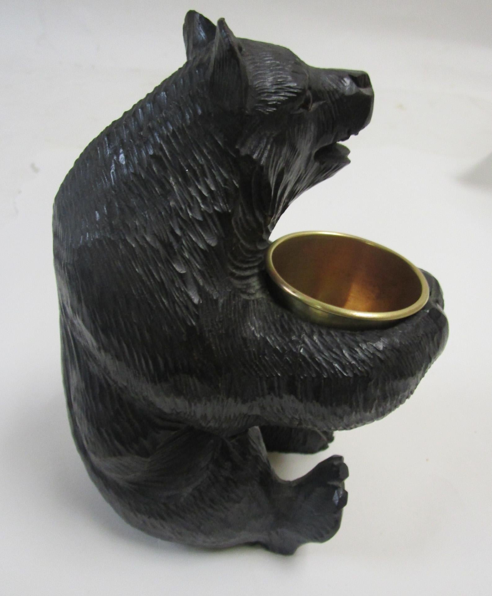 This whimsical hand carved seated wooden brown bear holds a brass cup suitable for cigarettes, matches or even a small bouquet of flowers. Very detailed carving with tiny teeth and a red painted tongue. Inserted glass eyes. A very charming fellow.