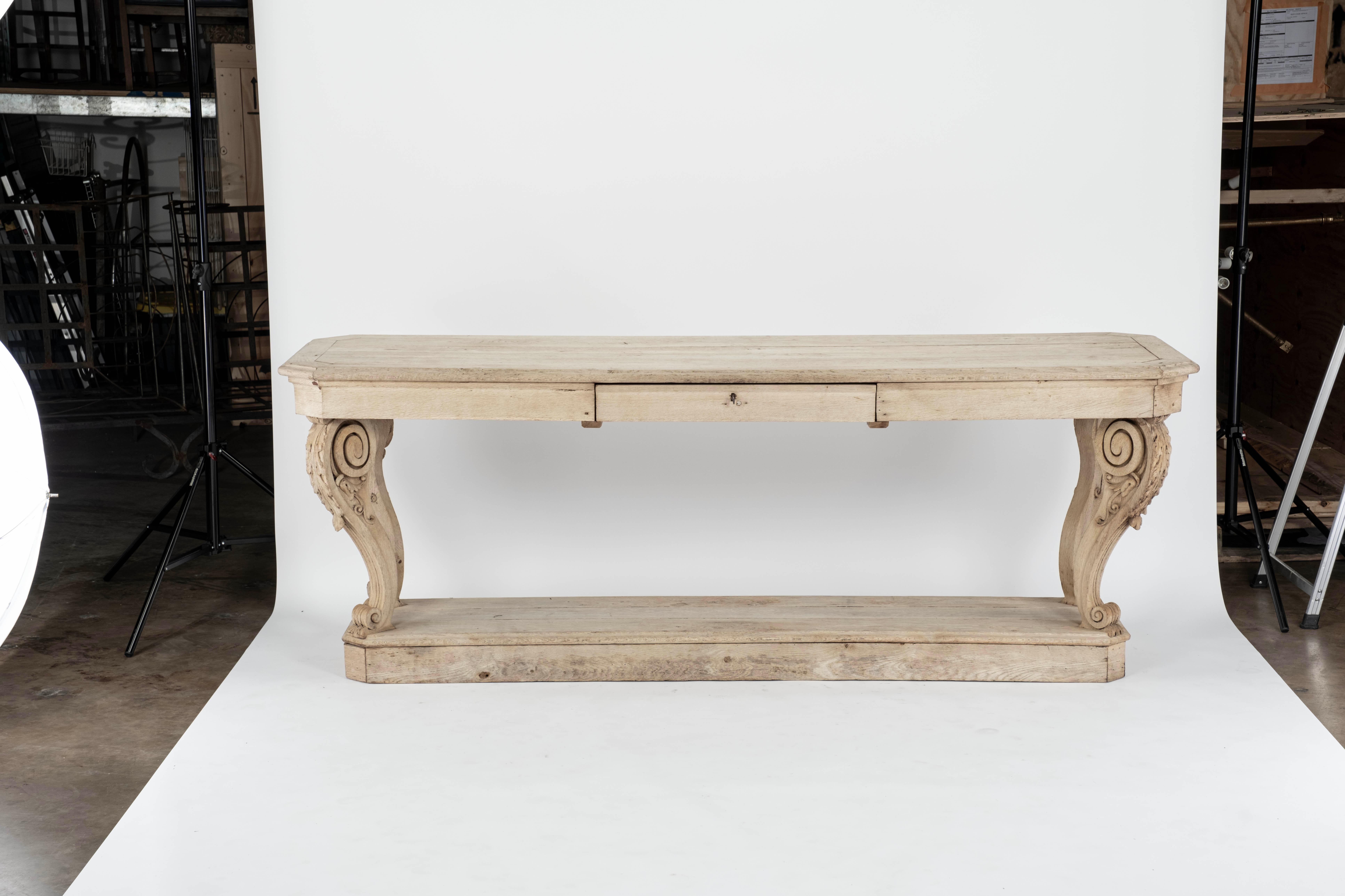 Bleached oak draper's table with a drawer and 4 carved scrolled legs sitting on a raised platform shelf.