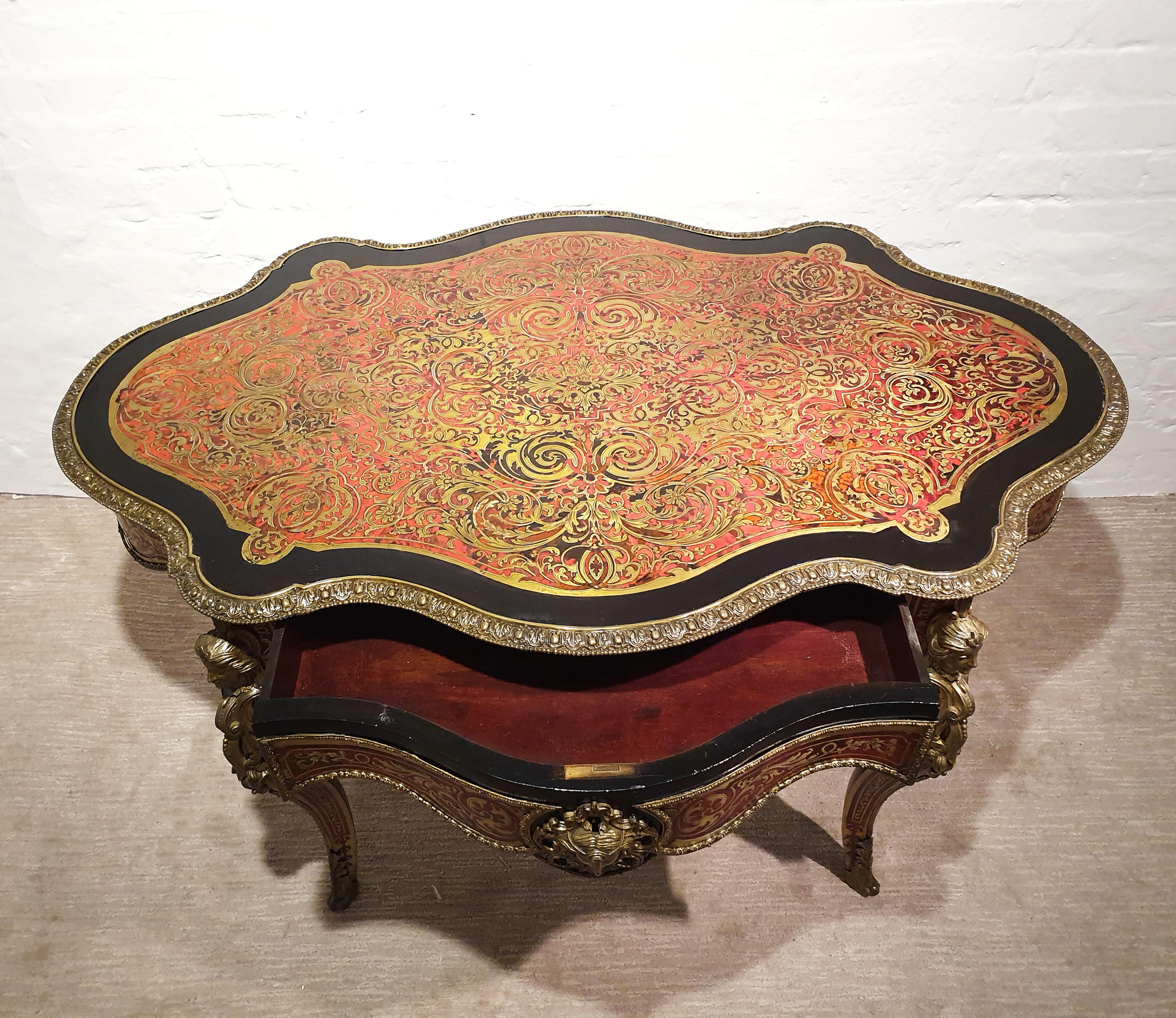 This magnificent and intricately detailed 19th century Boulle shaped center table features one central top drawer with a shaped skirt and ornate masks on each side, surrounded by an ebonised wood border around the top edge. The table is supported on