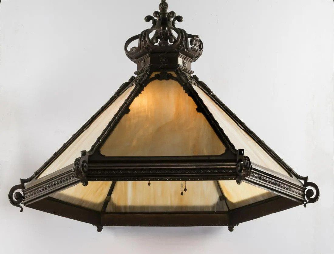 19th century patinated bronze hexagonal chandelier with inset art glass panels, having a fully formed French style crown canopy accented with fleur-de-lis and acanthus leaf details, surmounting six sloping sides interspersed with acanthus leaf