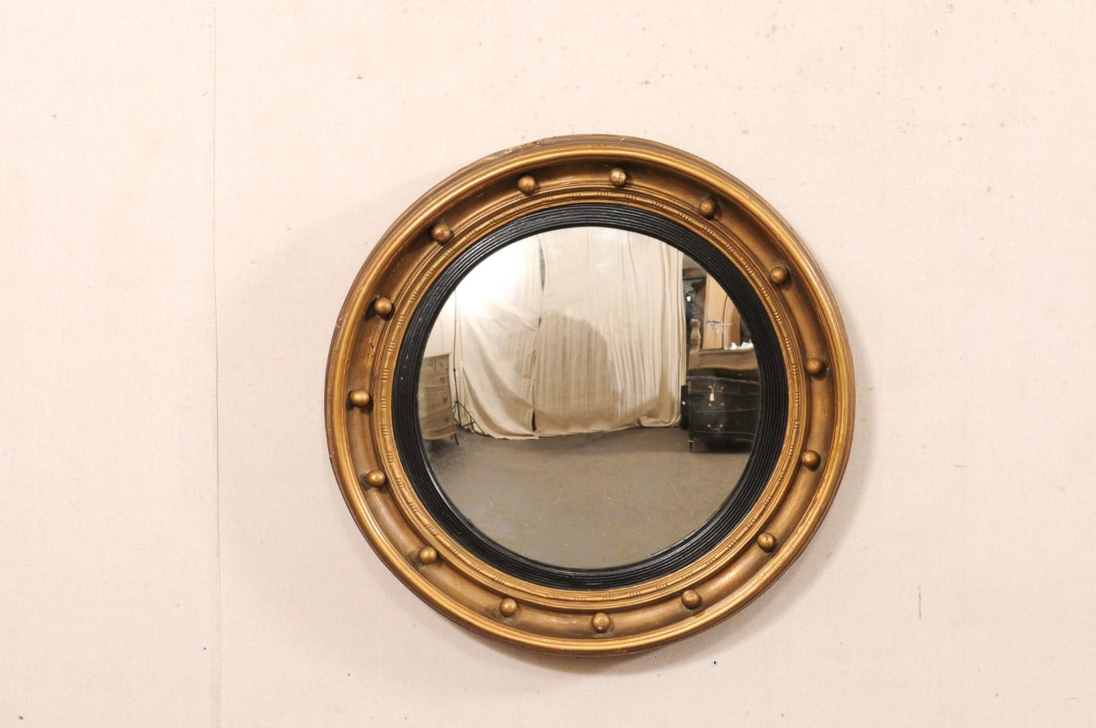 An American carved-wood bullseye accent mirror in black and bronze/gold, from the 19th century. This antique mirror features a round/convex glass center, set within in circular carved-wood frame, adorned with small spheres, rhythmically spread out