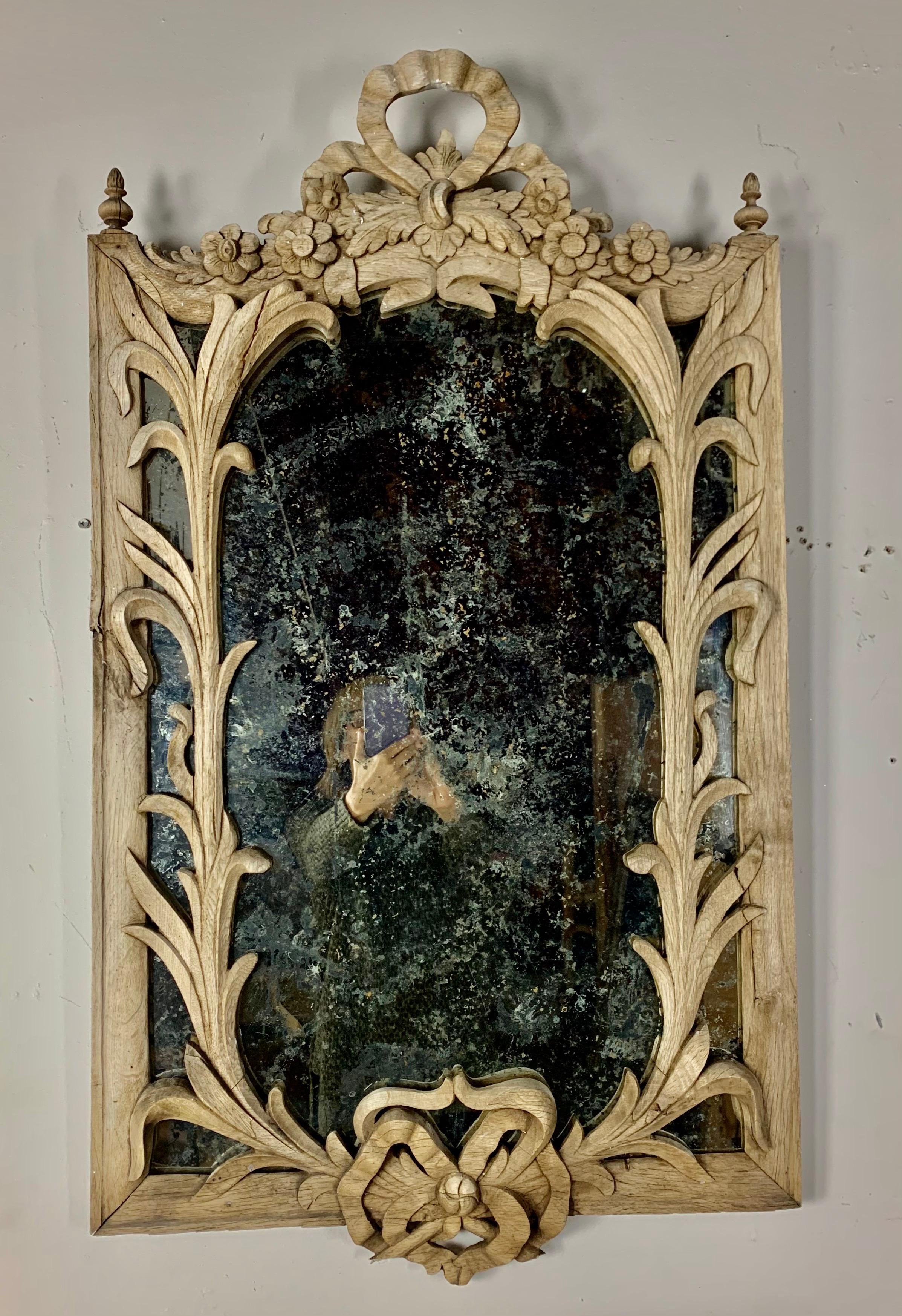 19th century carved French bleached oak mirror with leaves and bows throughout. The oak has been bleached into a beautiful coloration and has an antiqued mirror inset.