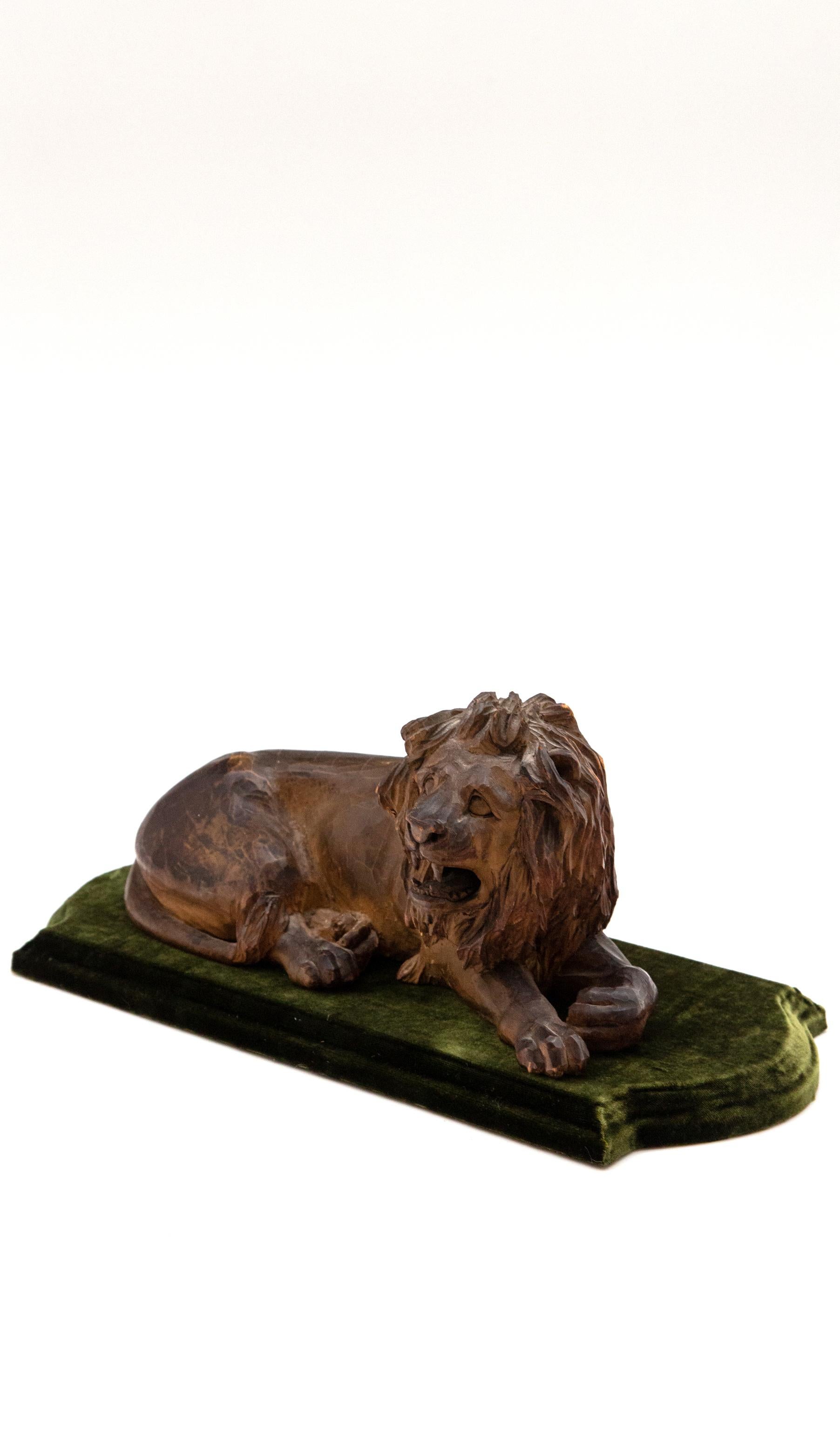 19th century carved wooden reclining lion on a green velvet base. Beautifully detailed hand carved lion resting on olive-green velvet-covered base. Measures: 14