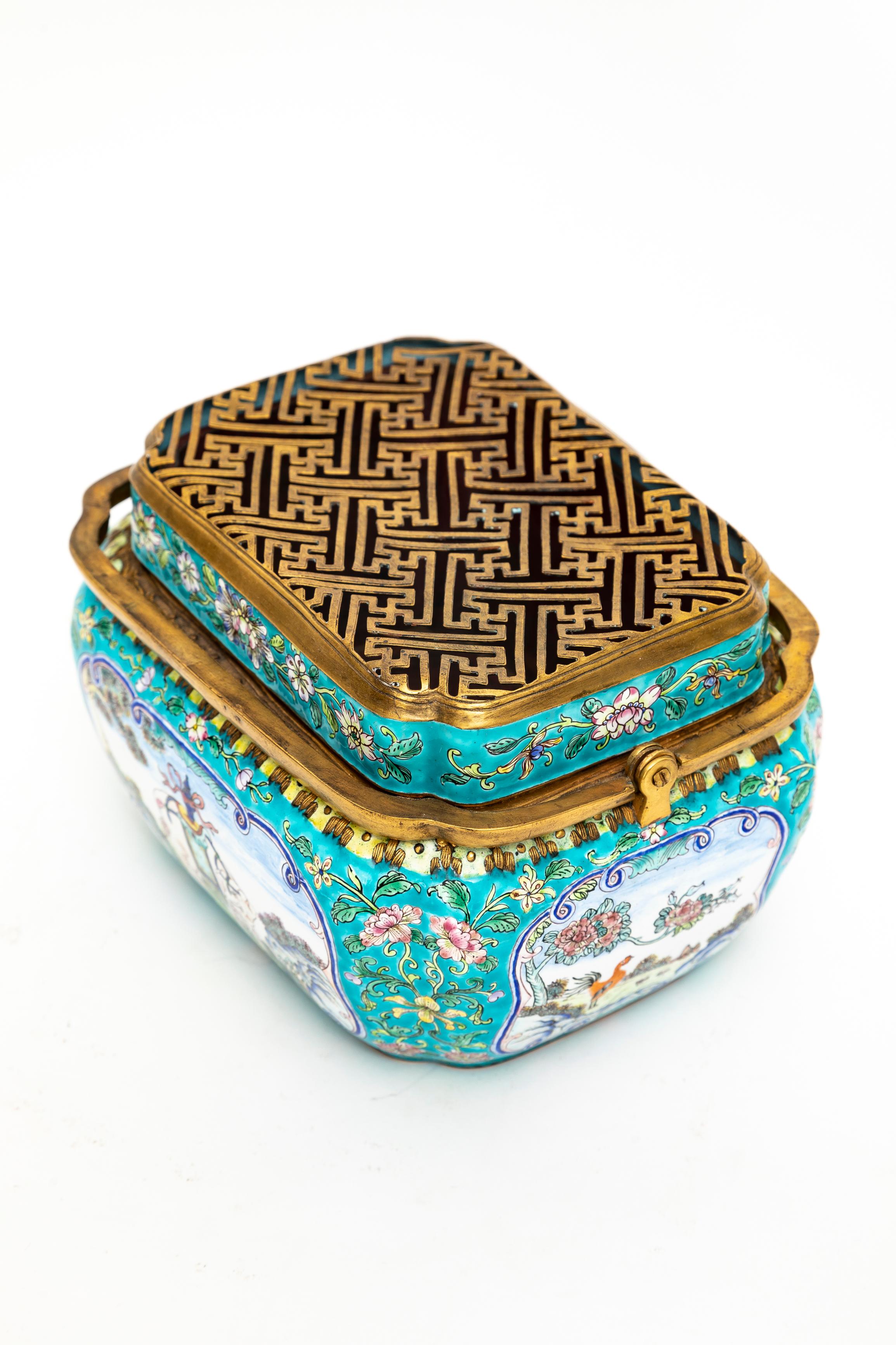 An Antique 19th Century Chinese Canton Enamel Gilt Bronze Mounted Hand-Warmer With Double Handle

A rectangular Canton enamel hand-warmer with rounded corners, featuring a hinged double handle and a removable pierced cover. The body is decorated