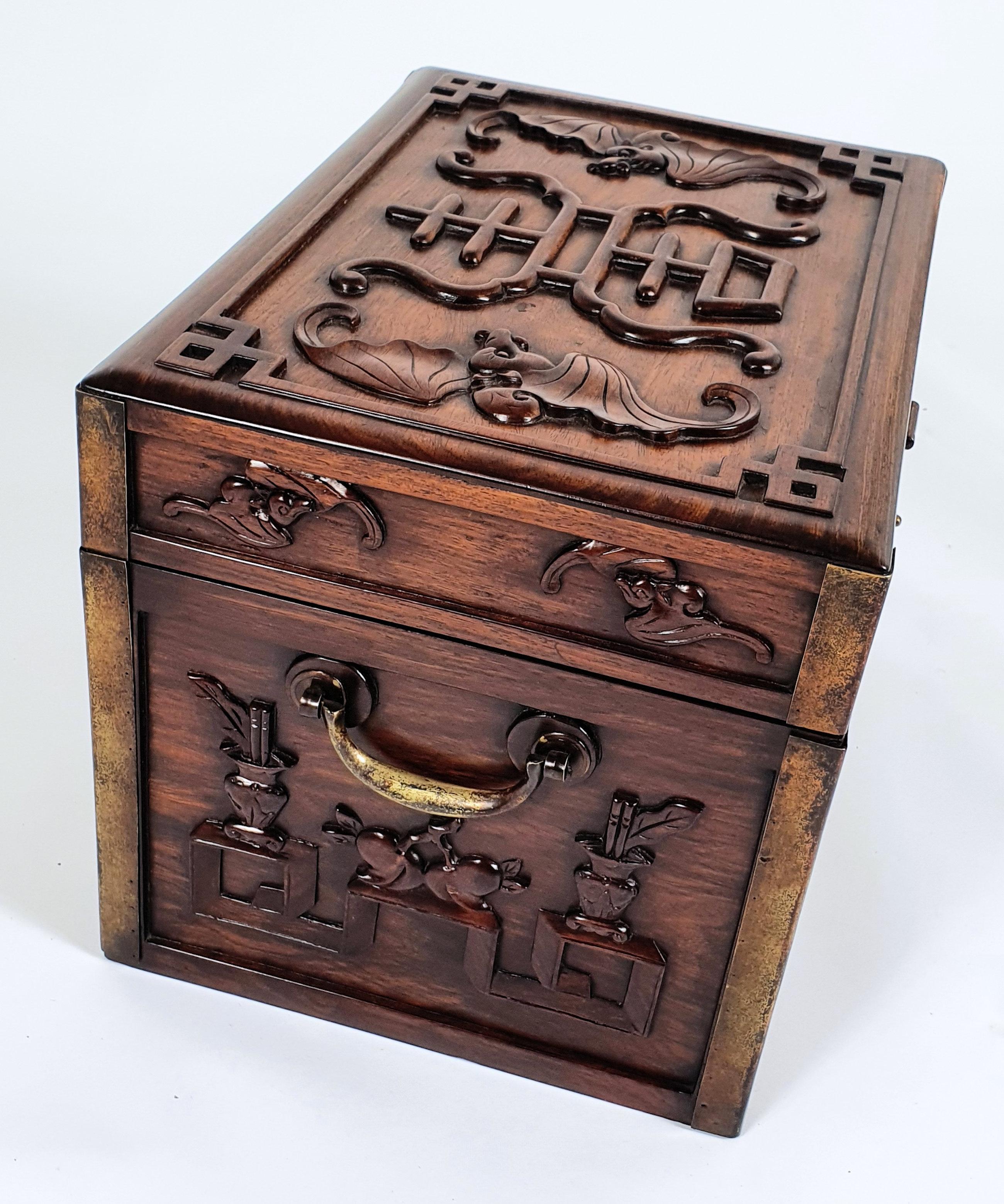 This magnificent and ornately carved 19th century Chinese carved hardwood documents box features brass corners, hinges and lock. It is decorated with bats, jardinières of flowers and precious objects.
The box measures 16 ¾ in – 42.5 cm wide, 12 in