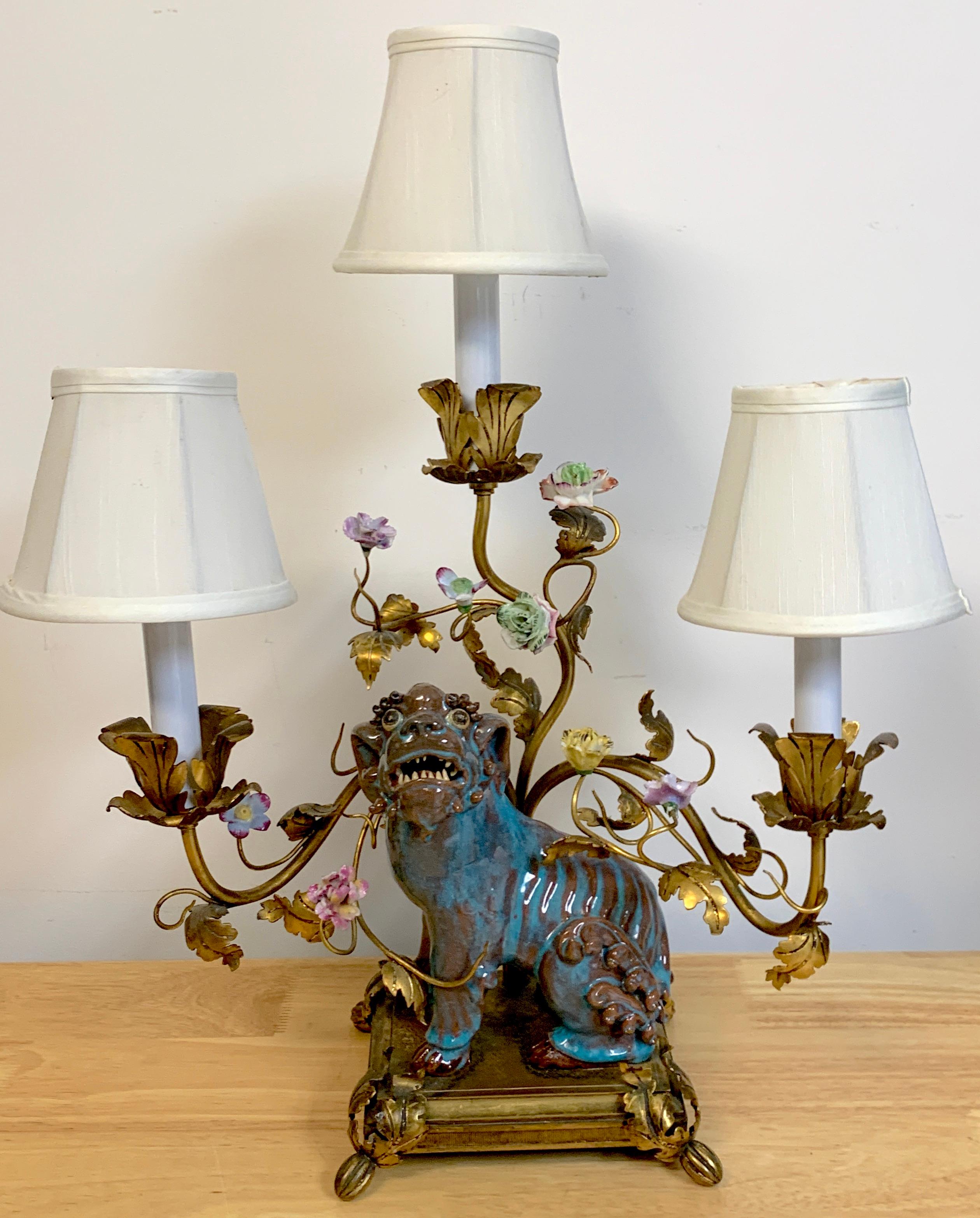 Late Qing Chinese Expot Fu Dog mounted with French bronze mounts as a lamp, Shiwan glazed seated Fu dog surrounded with French porcelain flowers, and three candelabra lights, raised on a bronze base with
The base measures 7.5