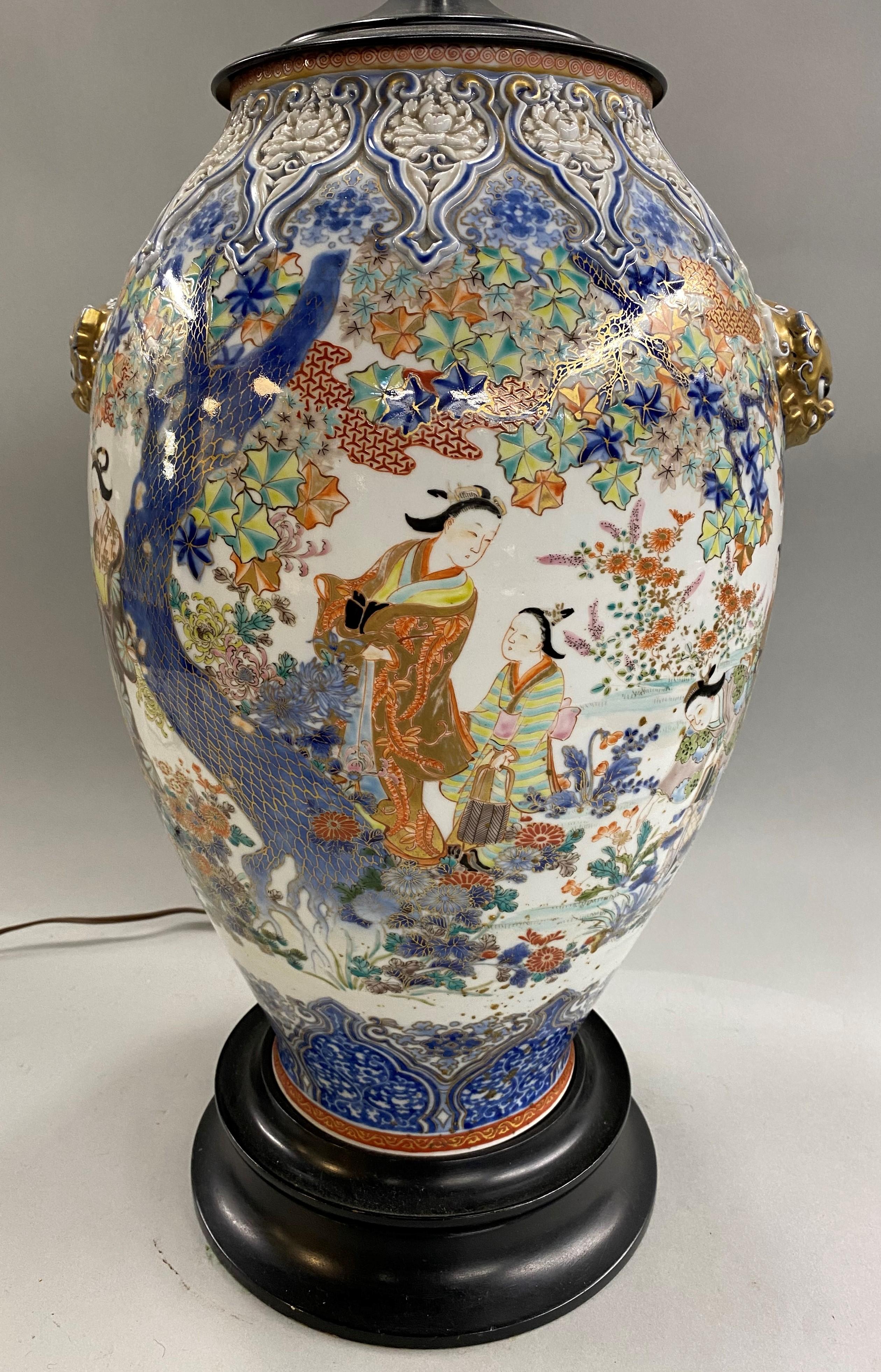 A fine Chinese polychrome porcelain converted vase lamp with geometric decoration around the top and bottom flanking a central panel with traditional figures, trees, and foliate decoration, gilt foo dog handles on each side, an ebonized molded base