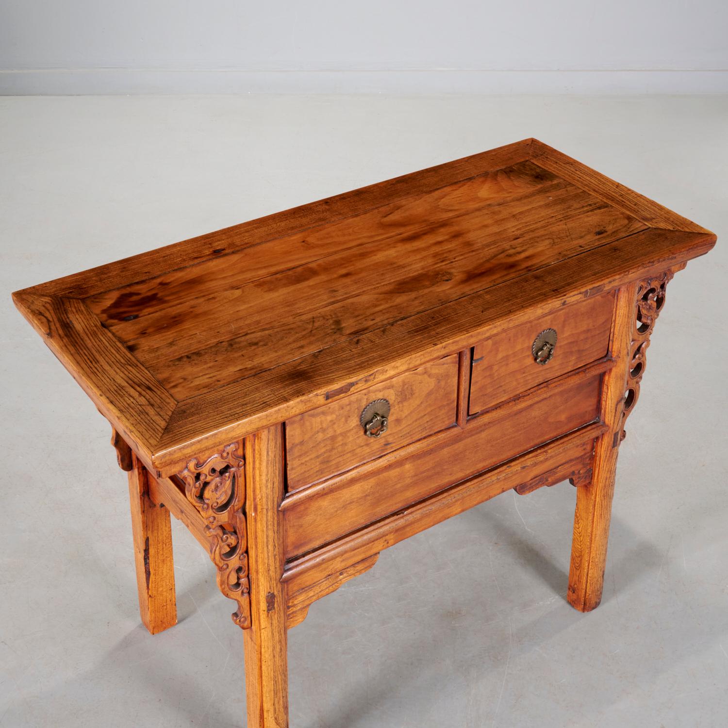Qing Dynasty (19th c), an elm wood, two drawer, altar coffer with brass flower-shaped ring pulls. The rectangular top sits over two frieze drawers above a plank panel and shaped apron, flanked by pierced openwork scrolling cloud molding, the whole