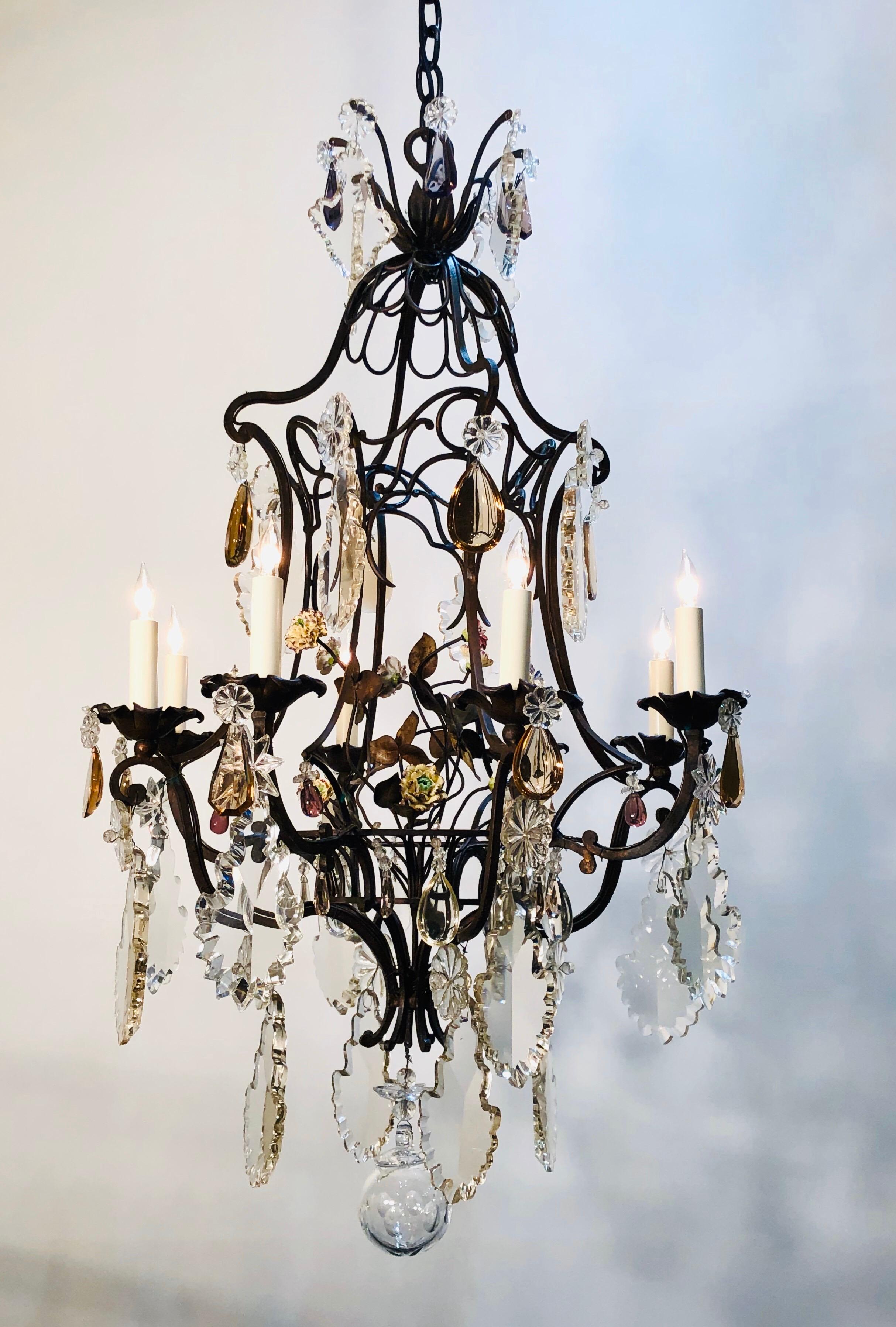 This beautiful French wrought iron chandelier has a bird cage frame with a scrolled pagoda crown. The center of the bird cage has a basket with iron and porcelain flowers. The eight iron arm were originally candle and have been French wire and