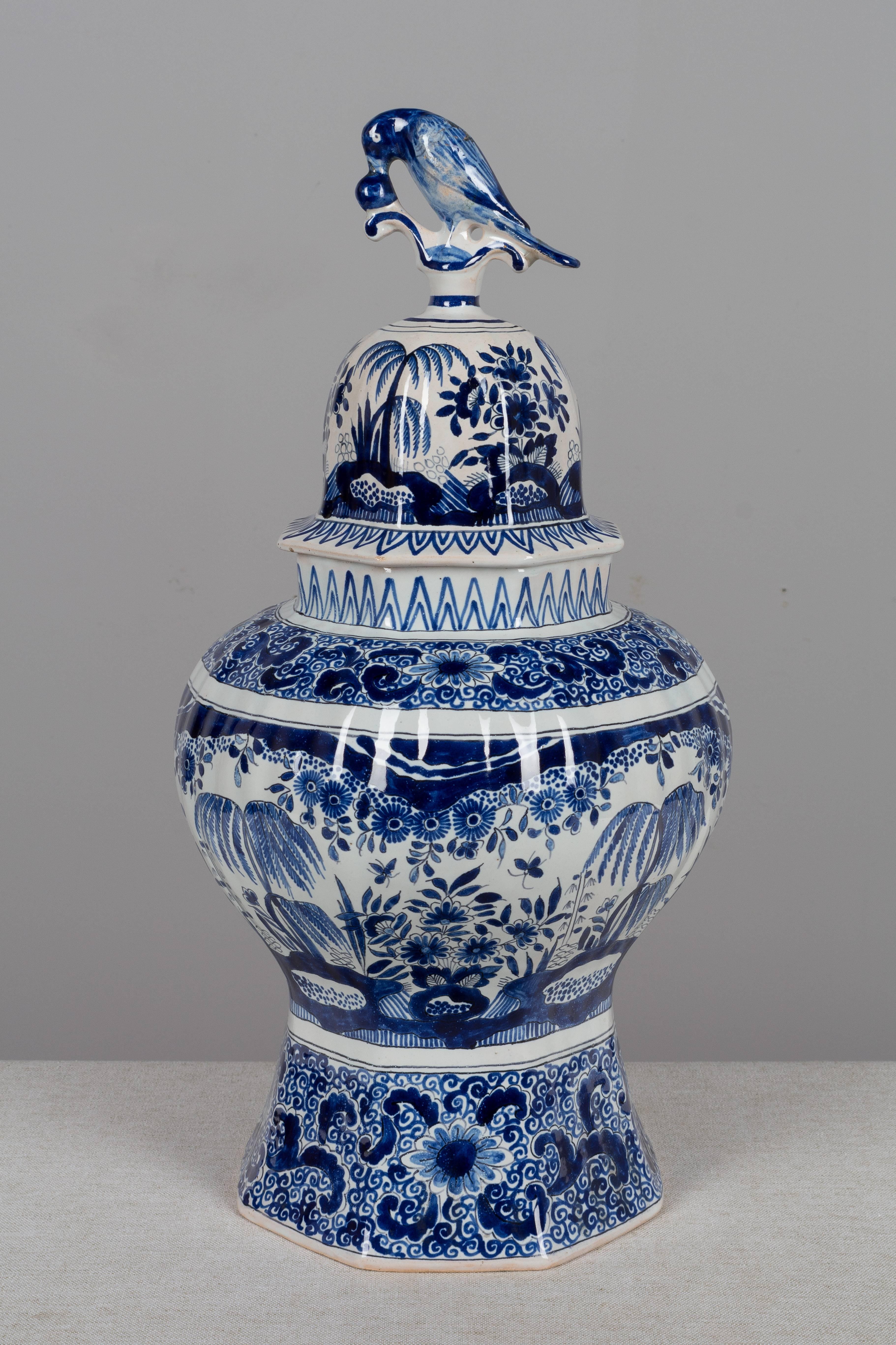 A large 19th century delft faience octagonal ginger jar with hand-painted blue floral decoration in the Asian manner. Domed lid with a bird perched on top. Small flaw in glazing of the top of the bird and repair to the tail. Please refer to photos
