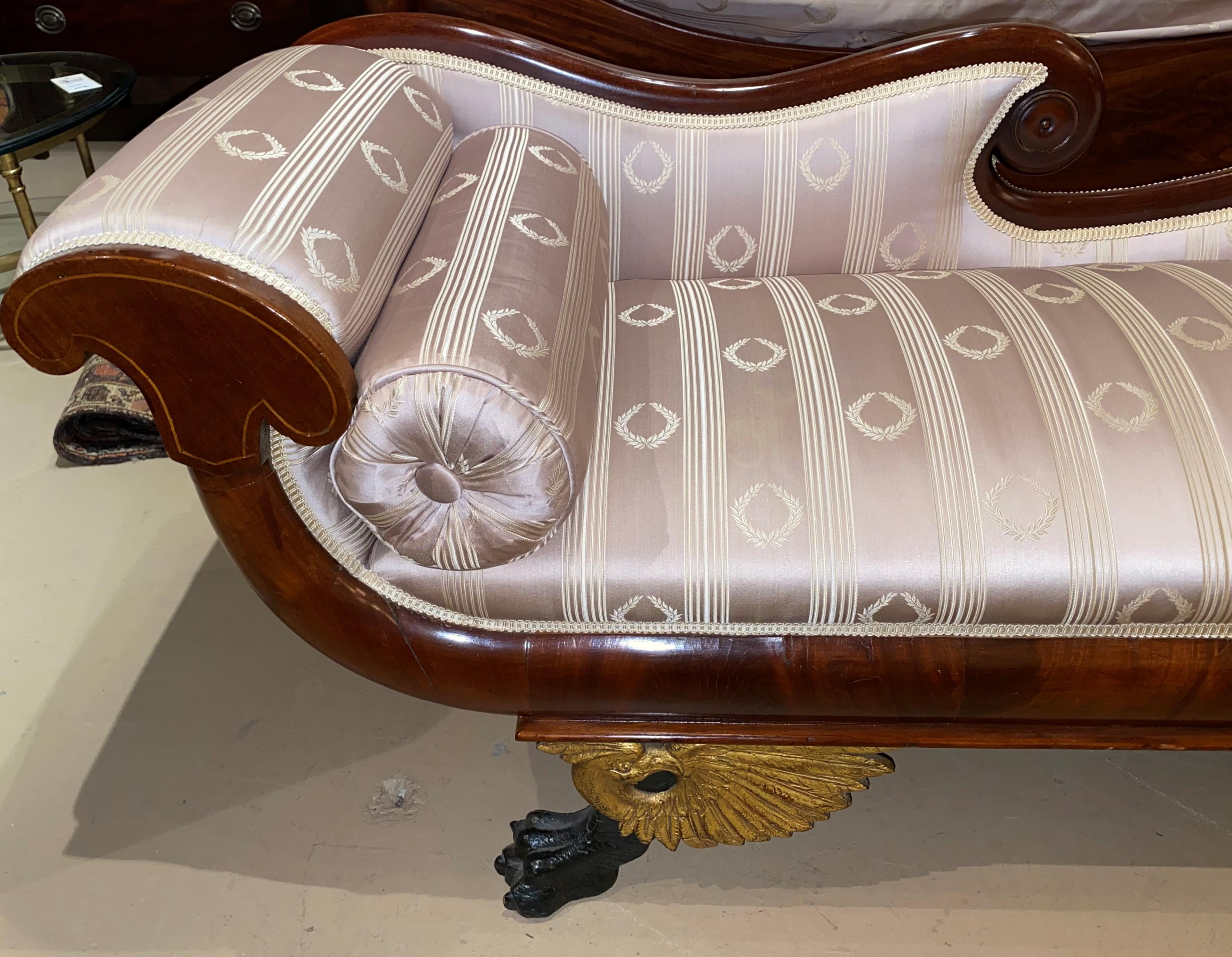 A beautiful diminutive Empire mahogany recamier with gilt eagle and ebonized claw feet, freshly appointed with satin upholstery all around, including a fitted cylinder pillow. Dating to the 19th century in very good restored condition, with minor