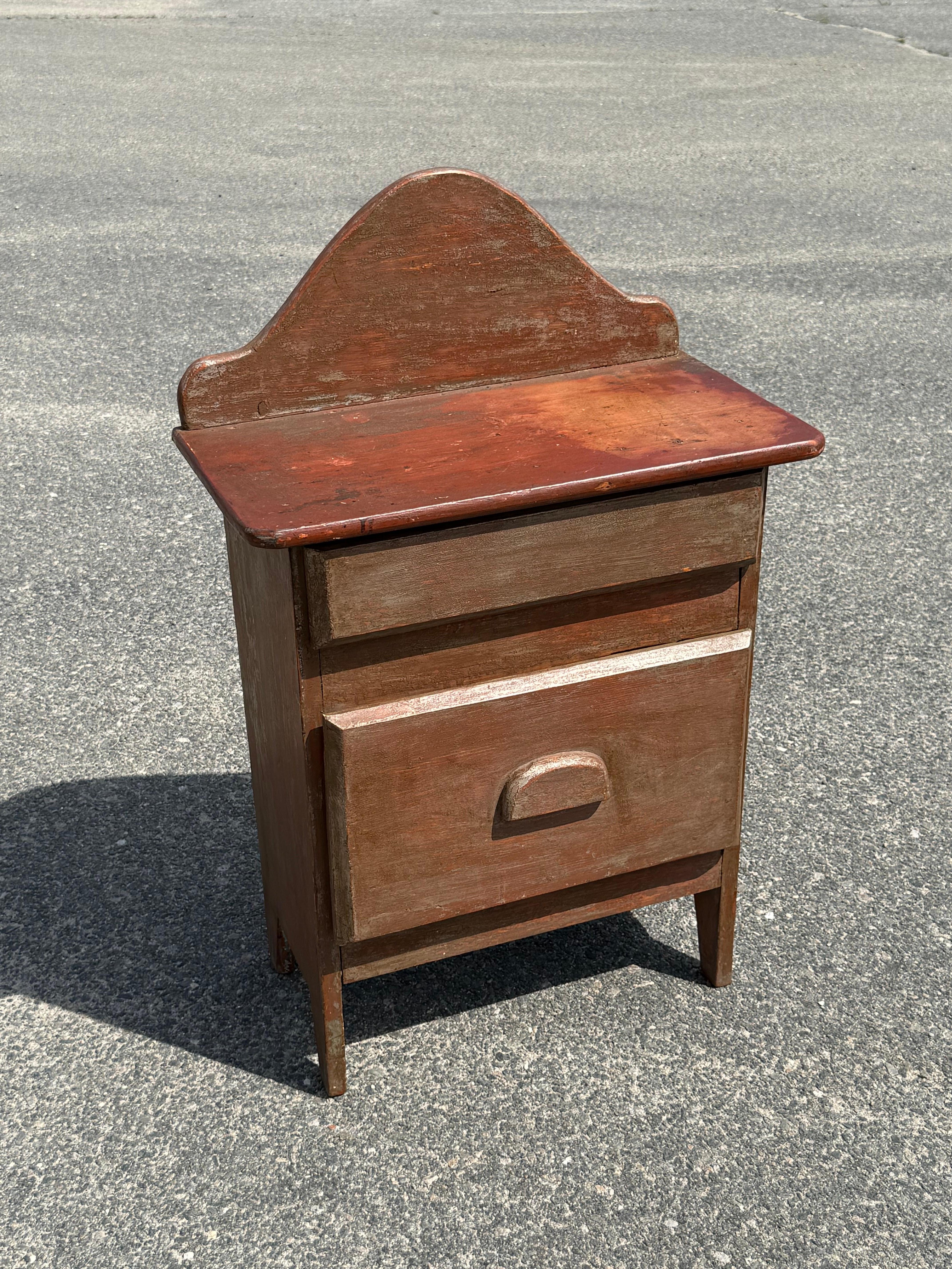 Diminutive 19th century two drawer chest in original paints.  A country piece crafted from thick pine boards with a exaggerated, arched backsplash, wooden surface (25