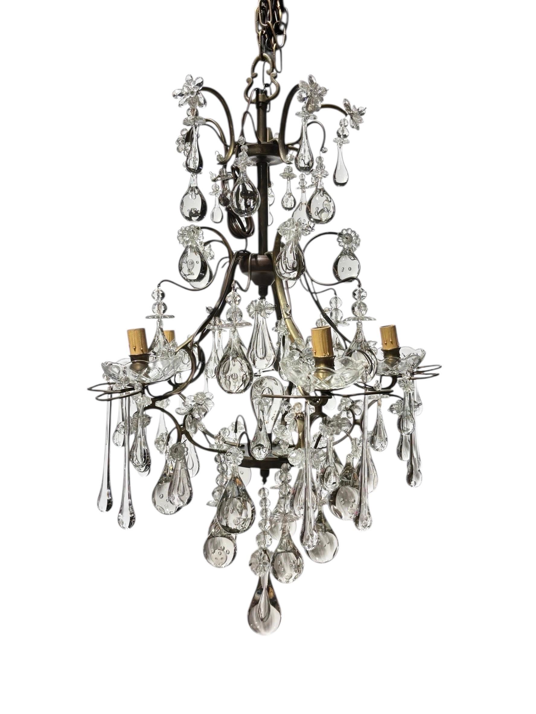 Una araña de latón y cristal de principios del siglo XIX. El elegante marco soporta gotitas de vidrio soplado a mano y flores de cristal, con candelabros sobre bobeches de cristal tallado. Diseñada originalmente para sostener velas, la araña ha sido